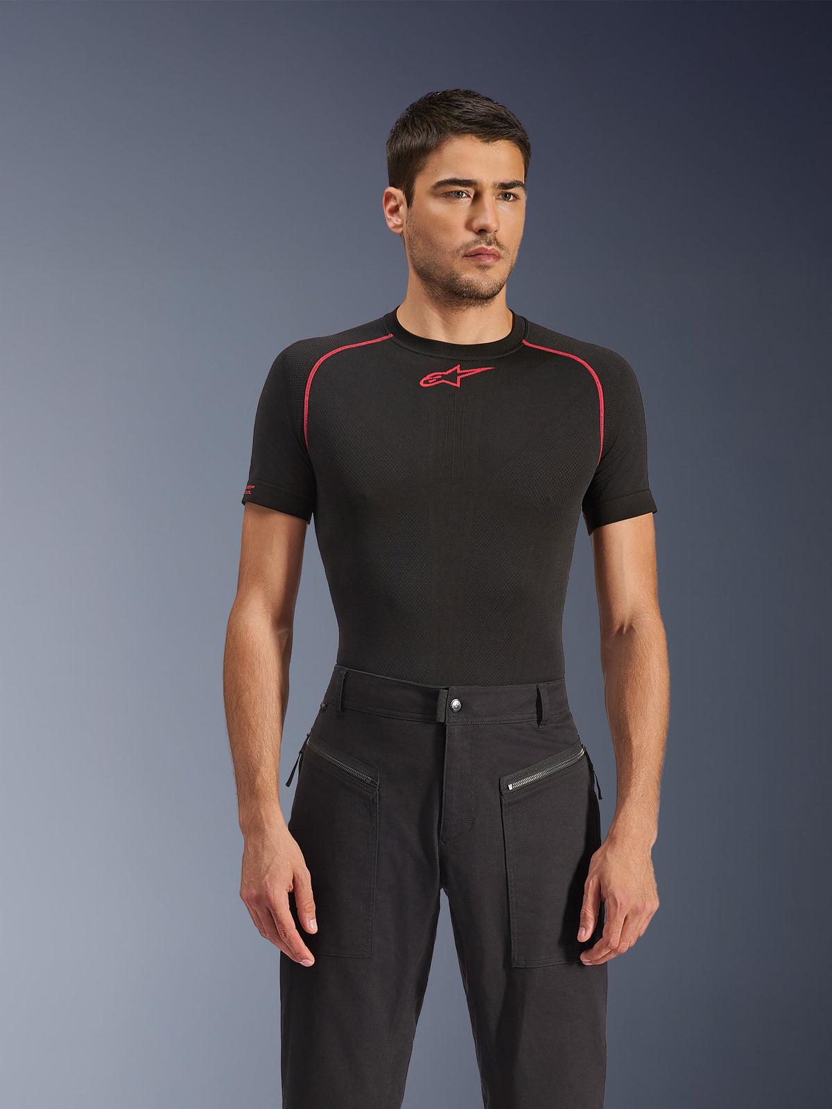 Modèle masculin portant le pantalon Alpinestars Flex-AST Canvas en noir, pantalon de moto urbain doté de poches avant zippées visibles et d'un design inspiré du style workwear, associé à une couche de base noire avec des accents rouges.