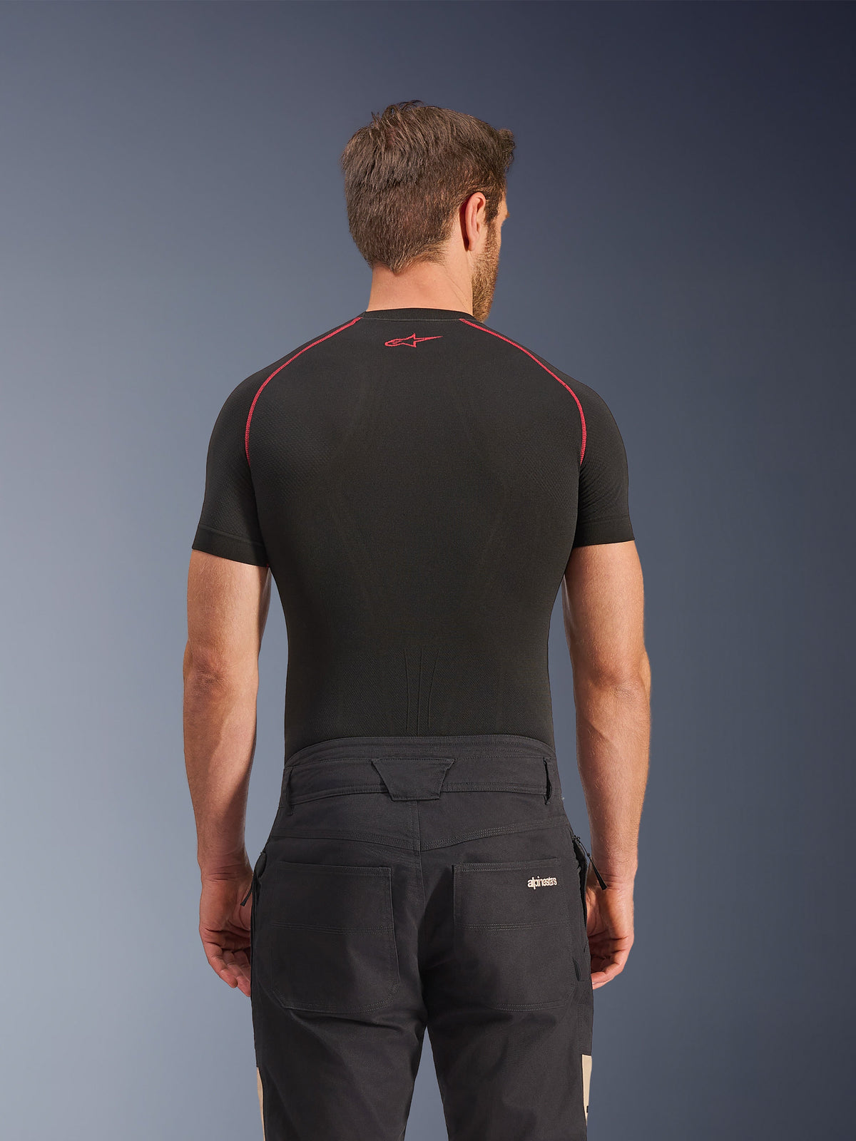 Pantalon Alpinestars Flex-AST Canvas en Black Aluminum, vue arrière sur modèle, pantalon de moto urbain d'inspiration workwear avec logo sur la poche arrière, associé à une couche de base noire à manches courtes avec surpiqûres rouges.