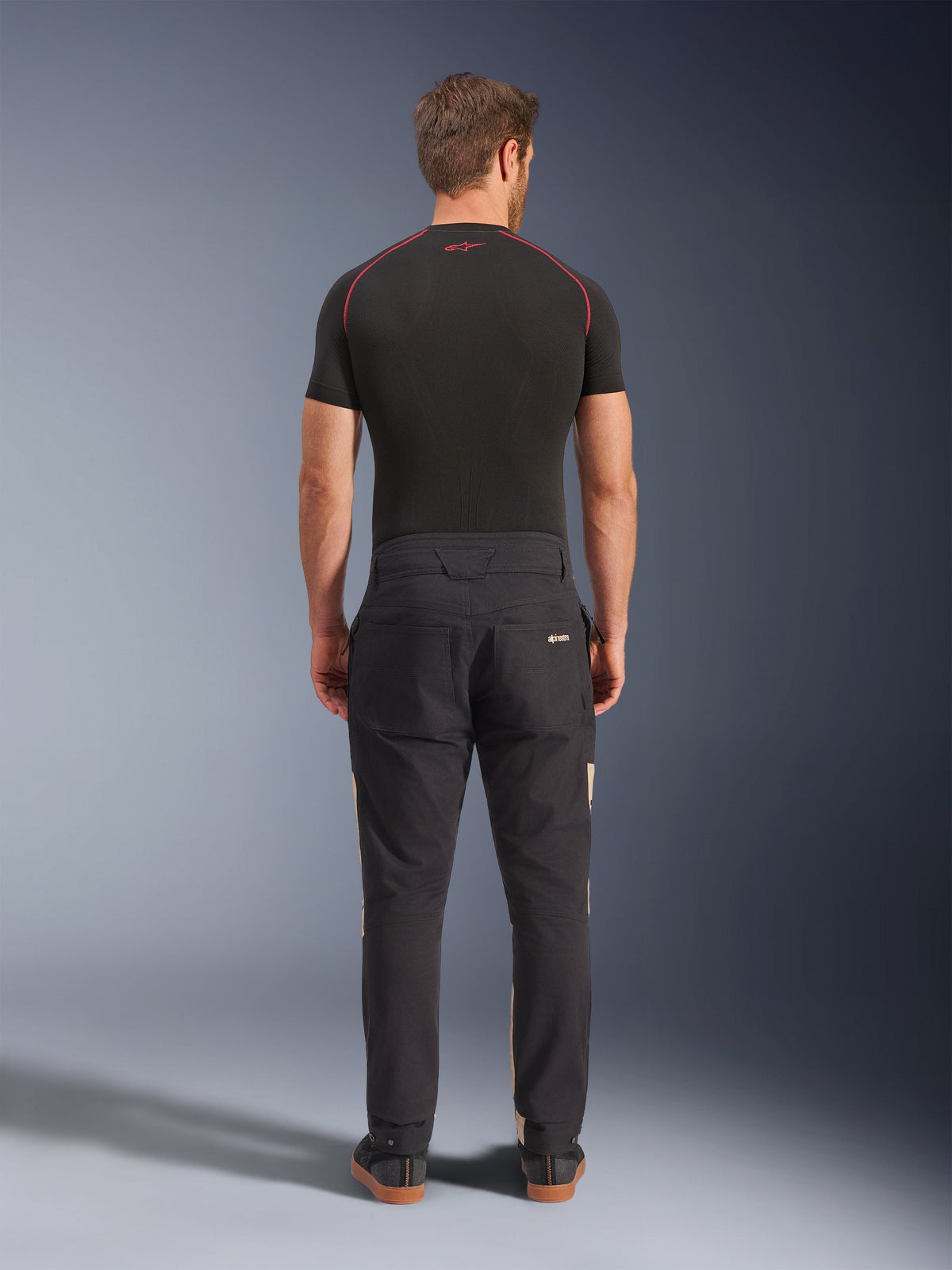 Pantalon Alpinestars Flex-AST Canvas en Black Aluminum, vue de dos sur un mannequin, style inspiré du workwear avec poches arrière et empiècements latéraux beiges discrets, porté avec une couche de base technique noire et des baskets de moto décontractées.