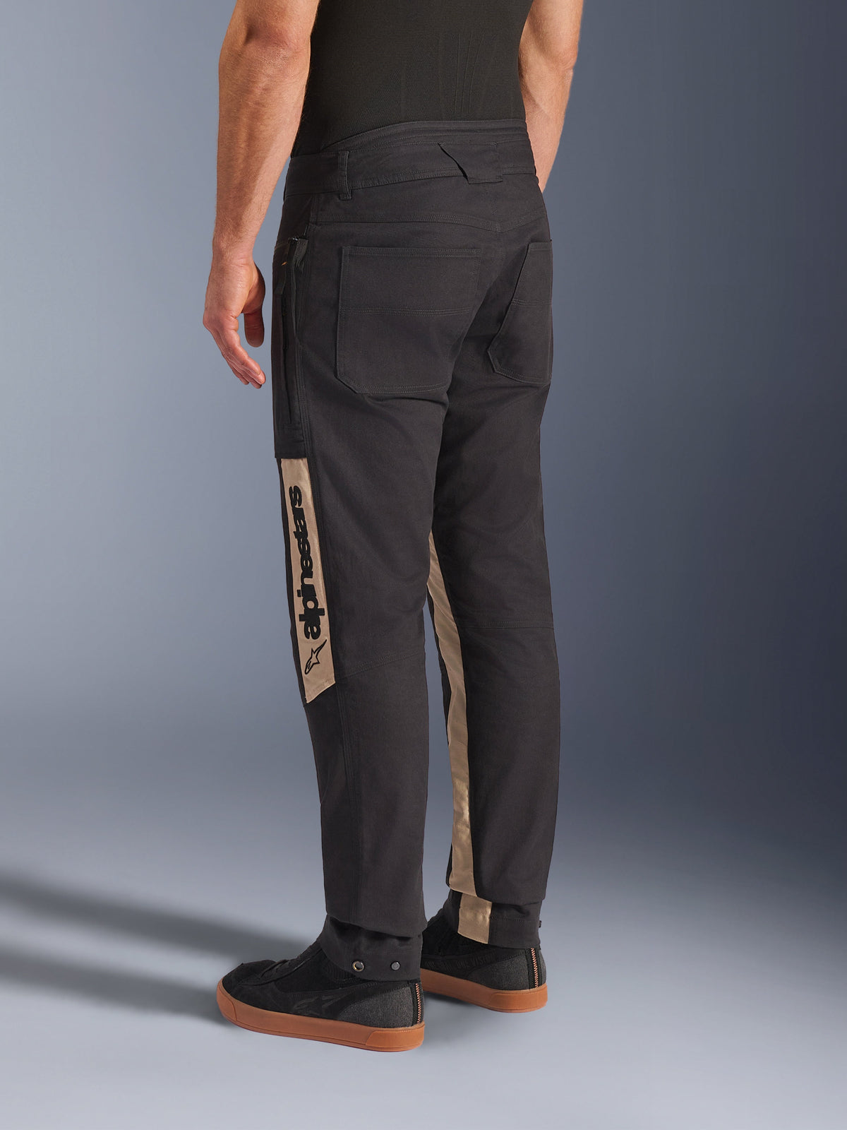 Pantalon Alpinestars Flex-AST Canvas en Black Aluminum, vue de dos montrant un pantalon de moto urbain avec de grandes poches inspirées du style workwear et des empiècements verticaux beiges sur les jambes arborant le logo Alpinestars.