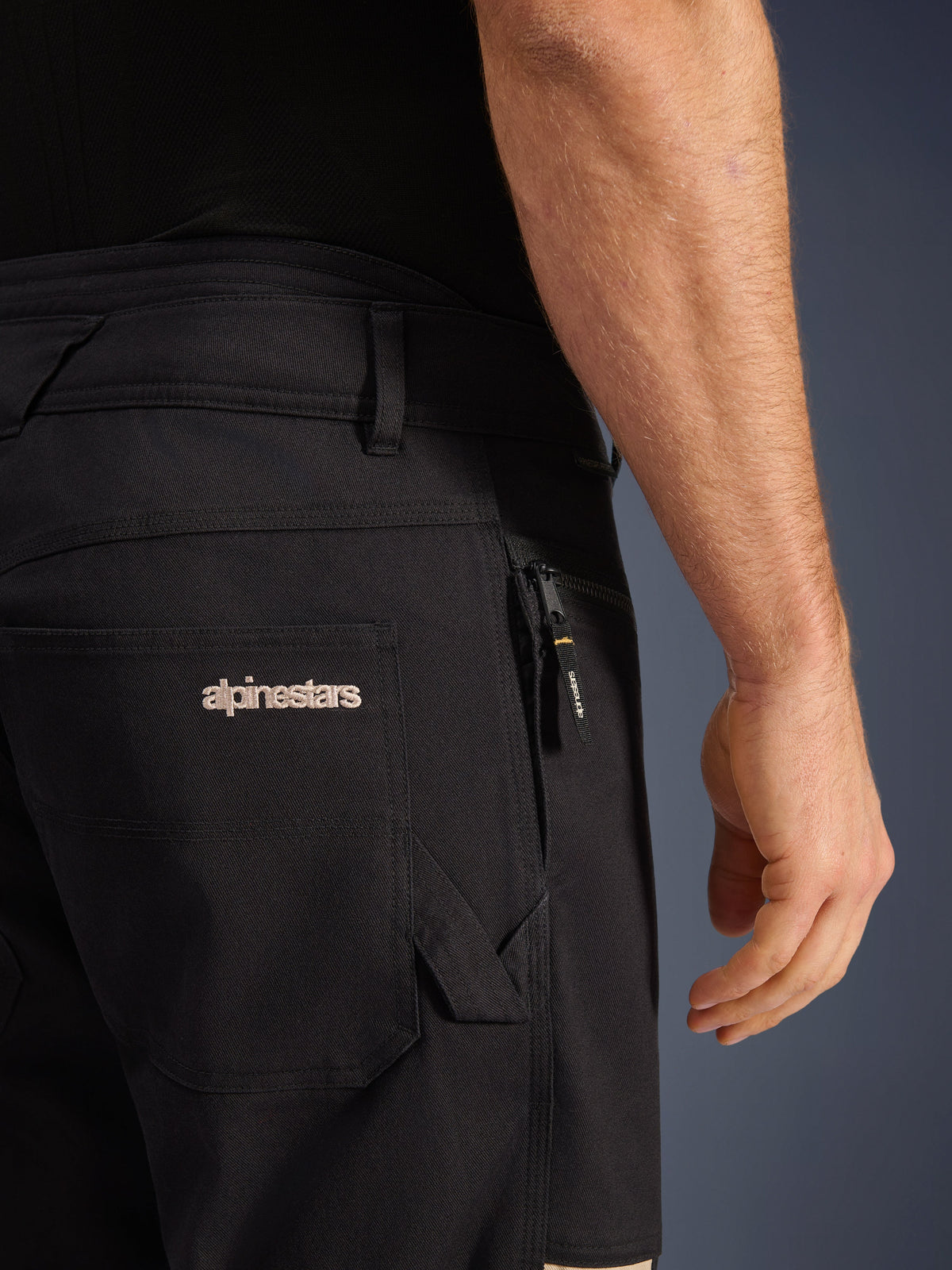 Pantalon Alpinestars Flex-AST Canvas, pantalon de moto urbain, Black Aluminum, gros plan sur les poches arrière et latérales, arborant le logo Alpinestars brodé, poche zippée avec tirette de marque, construction en sergé de toile extensible durable.