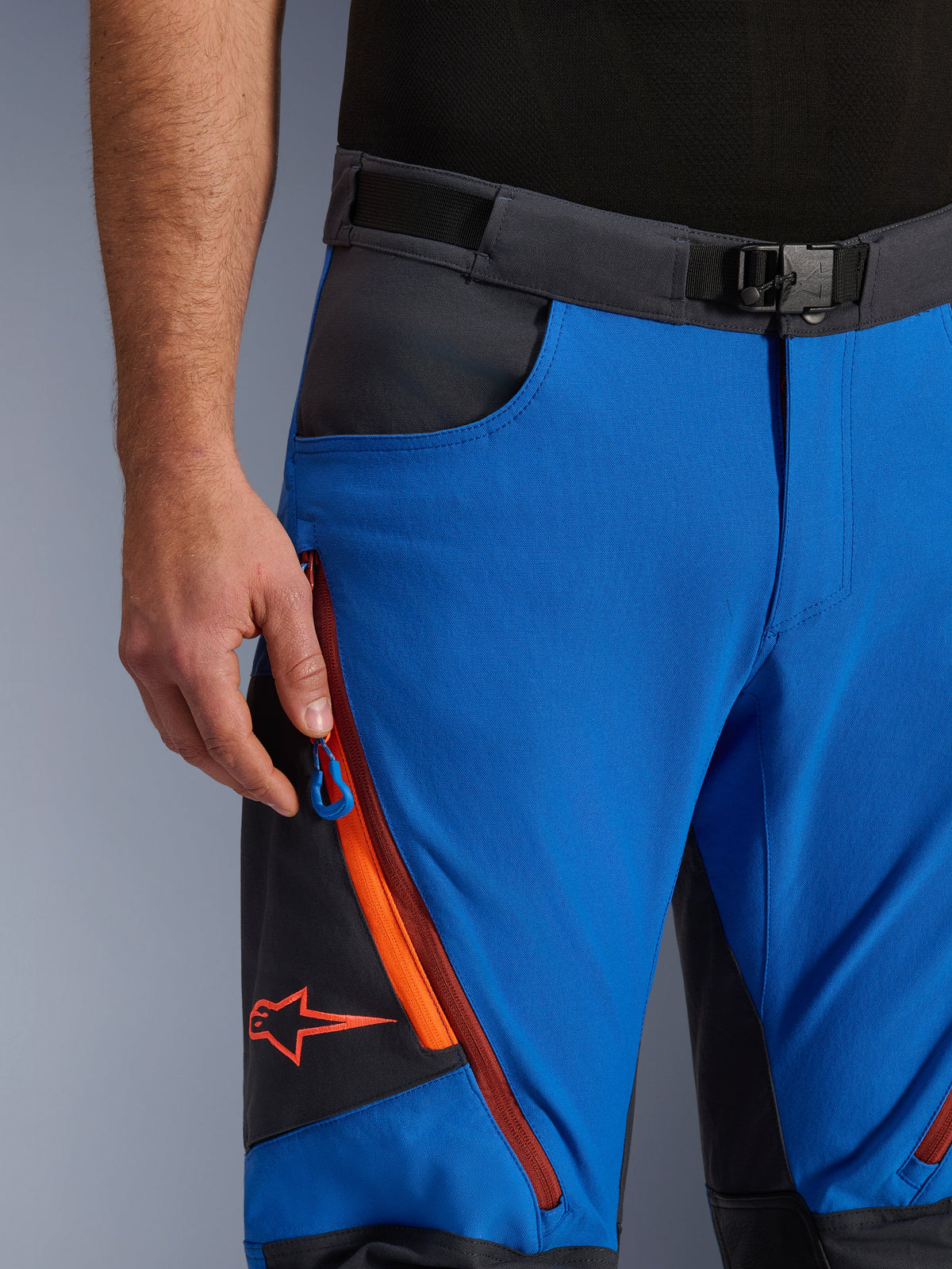 Alpinestars Maxdura Dual Pants in Royal Blue and Deep Gray, close-up view of the waistband with magnetic buckle, zippered cargo pocket with orange detailing and red Alpinestars logo, technical adventure motorcycle riding gear