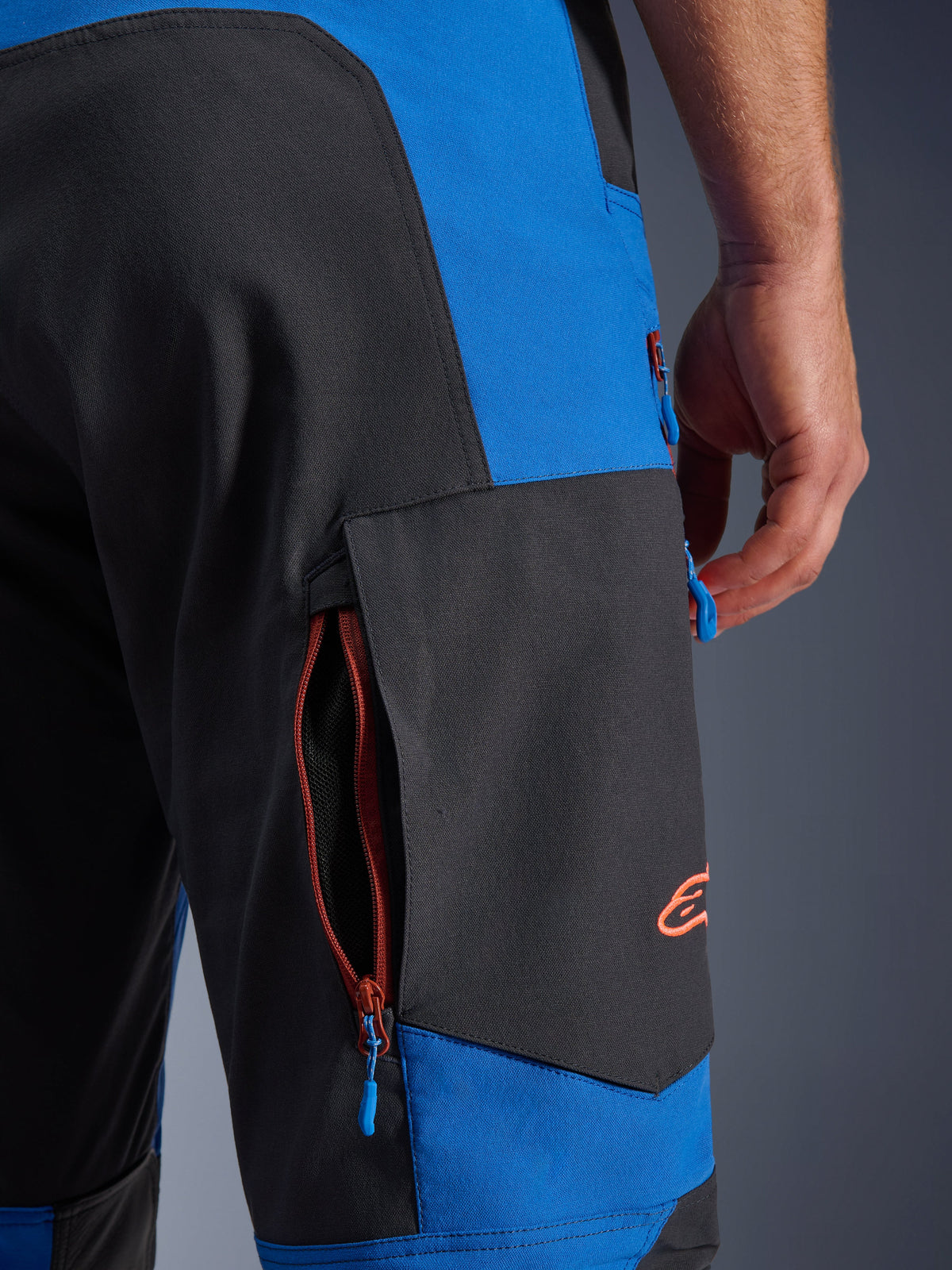 Alpinestars Maxdura Dual Pants, Royal Blue and Deep Gray, close-up of side zippered cargo pocket, blue zipper pulls, orange embroidered logo, adventure motorcycle riding gear
