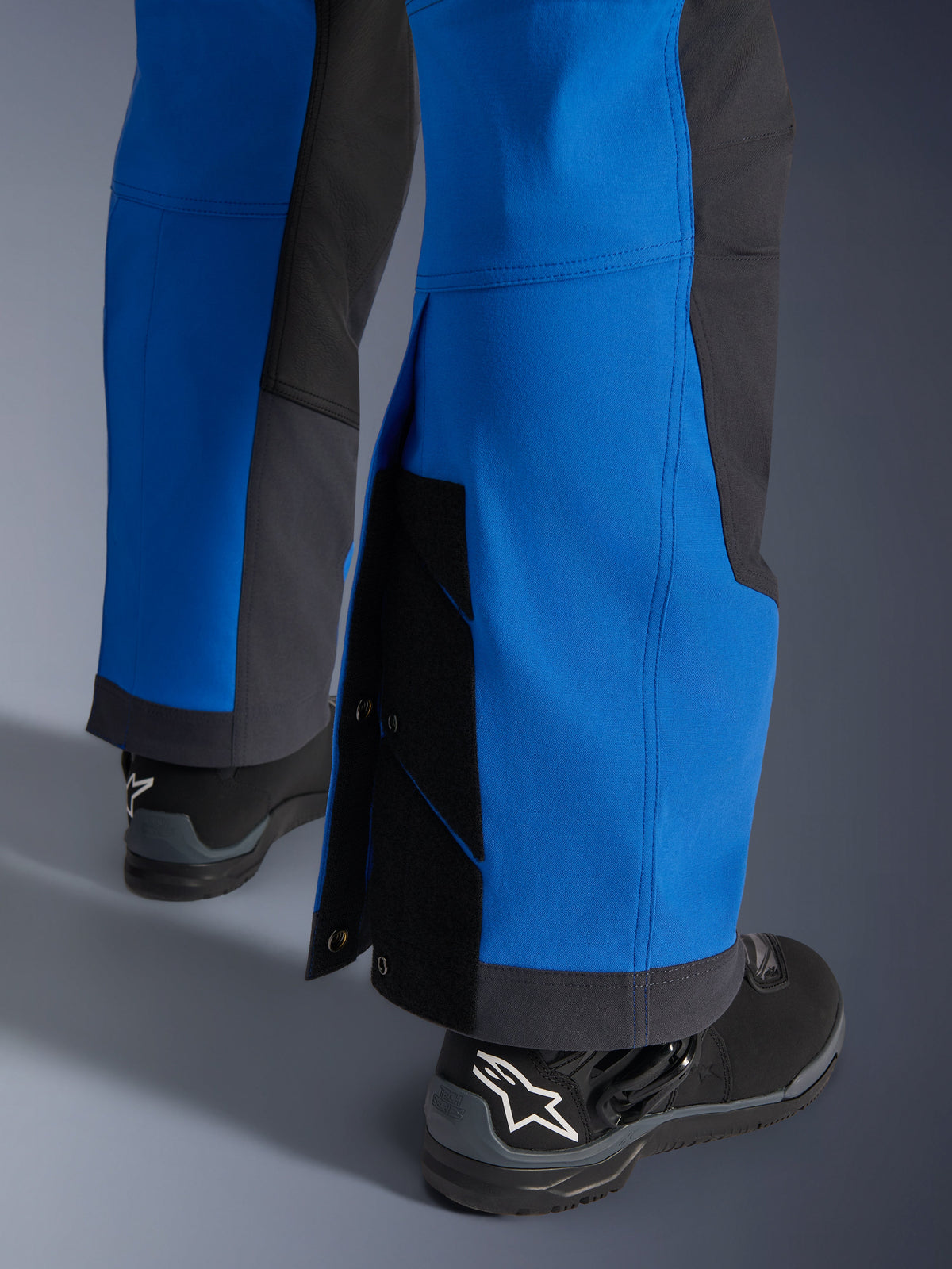 Alpinestars Maxdura Dual Pants, Royal Blue and Deep Gray, close-up of adjustable lower leg with snap closures and gusset, over-the-boot adventure fit design, worn with black Alpinestars motorcycle boots