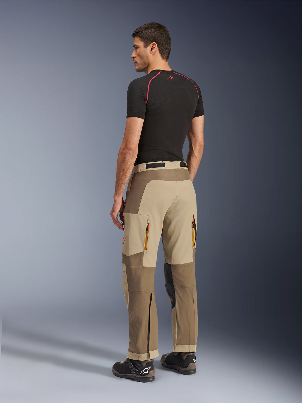 Alpinestars Maxdura Dual Pants, pantalon de moto aventure et dual-sport, Walnut Aluminum, vue arrière porté par un mannequin avec une couche de base noire et des bottes de moto, construction multi-panneaux avec évents arrière zippés et empiècements renforcés.