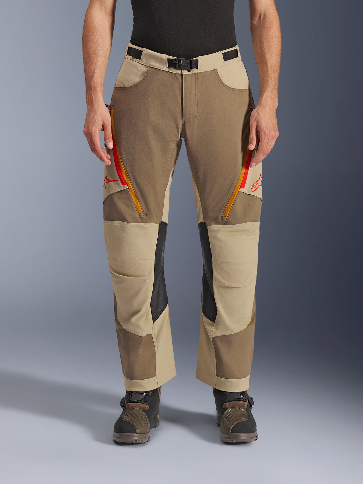Alpinestars Maxdura Dual Pants, Walnut Aluminum, pantalon de moto d'aventure avec évents zippés rouges et orange sur les cuisses, panneaux intérieurs aux genoux en cuir noir, porté avec une couche de base noire et des bottes robustes, design multi-tonal durable pour la conduite dual-sport