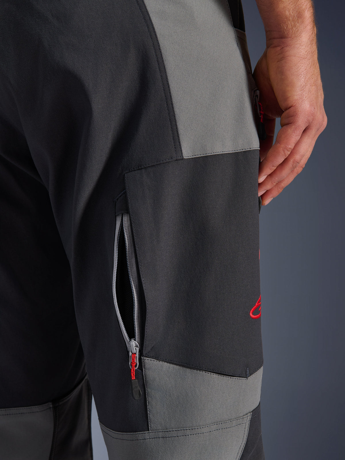 Alpinestars Maxdura Dual Pants, adventure motorbroek in donkergrijs en diepgrijs, close-up van de dij met een ventilatieopening met rits en rood geborduurd logo, duurzame stretch polyamide constructie
