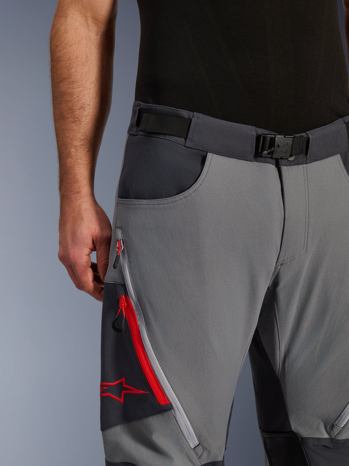 Alpinestars Maxdura Dual Pants, adventure motorbroek, donkergrijs en diepgrijs, close-up met verstelbare tailleband met magnetische gesp, cargozak met ritssluiting, rode details en Alpinestars-logo.
