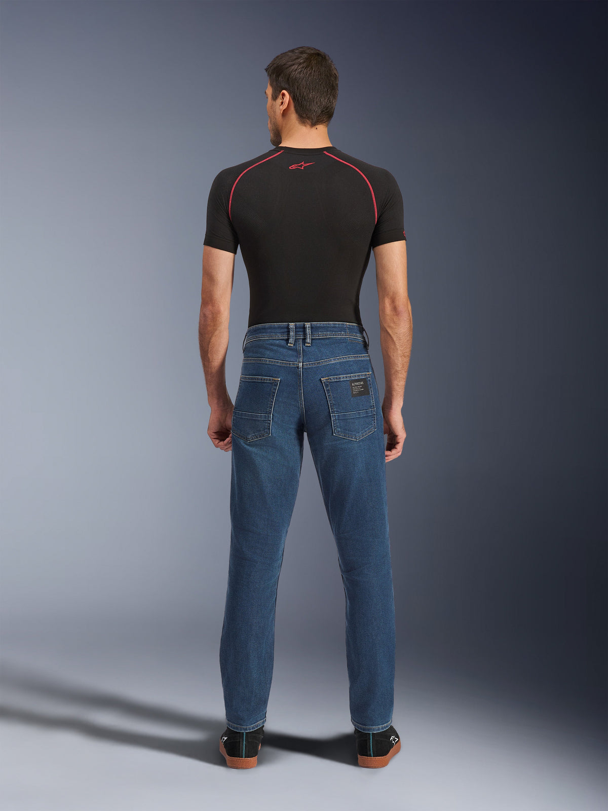 Alpinestars Flex-AST 5 Denim-Hose, Indigo Washed Blau, Rückansicht mit konisch zulaufender urbaner Passform, getragen von einem Modell mit schwarzem Performance-T-Shirt und Sneakern, lässige Motorrad-Schutzkleidung