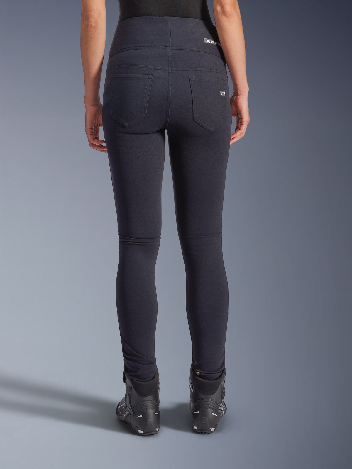 Alpinestars Stella Flex-AST Leggings, pantalon de moto urbain, noir, vue arrière présentant une coupe skinny taille haute, deux poches arrière fonctionnelles avec un marquage subtil, matière textile extensible, porté avec des chaussures de moto noires.