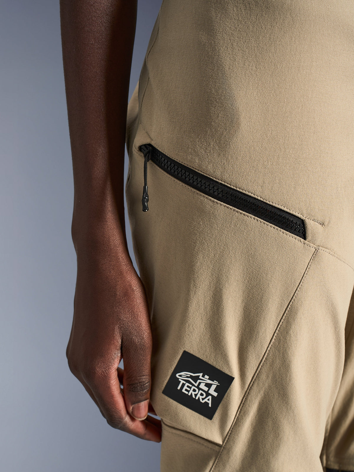 Alpinestars Stella Flex-AST Explorer broek, motorbroek voor dames, zandkleur, close-up van een cargozak met ritssluiting en zwarte ALL TERRA-logopatch, duurzame ripstop-textielconstructie voor adventure touring
