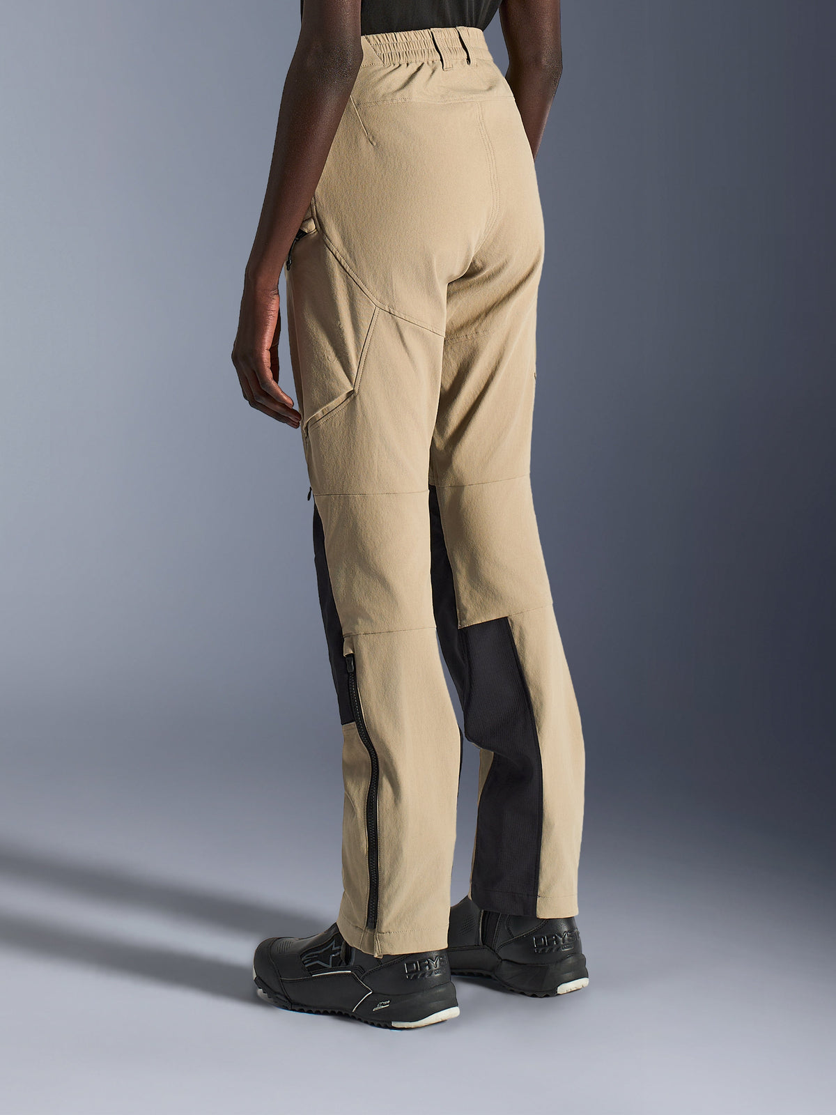 Alpinestars Stella Flex-AST Explorer Pants voor dames, motorbroek in zandkleur en zwart, achter- en zijaanzicht op een model, lichtgewicht ripstop-constructie, zwarte verstevigingspanelen aan de binnenkant van de kuiten, cargozakken met ritssluiting en ritsen aan de onderbenen voor adventure rijden