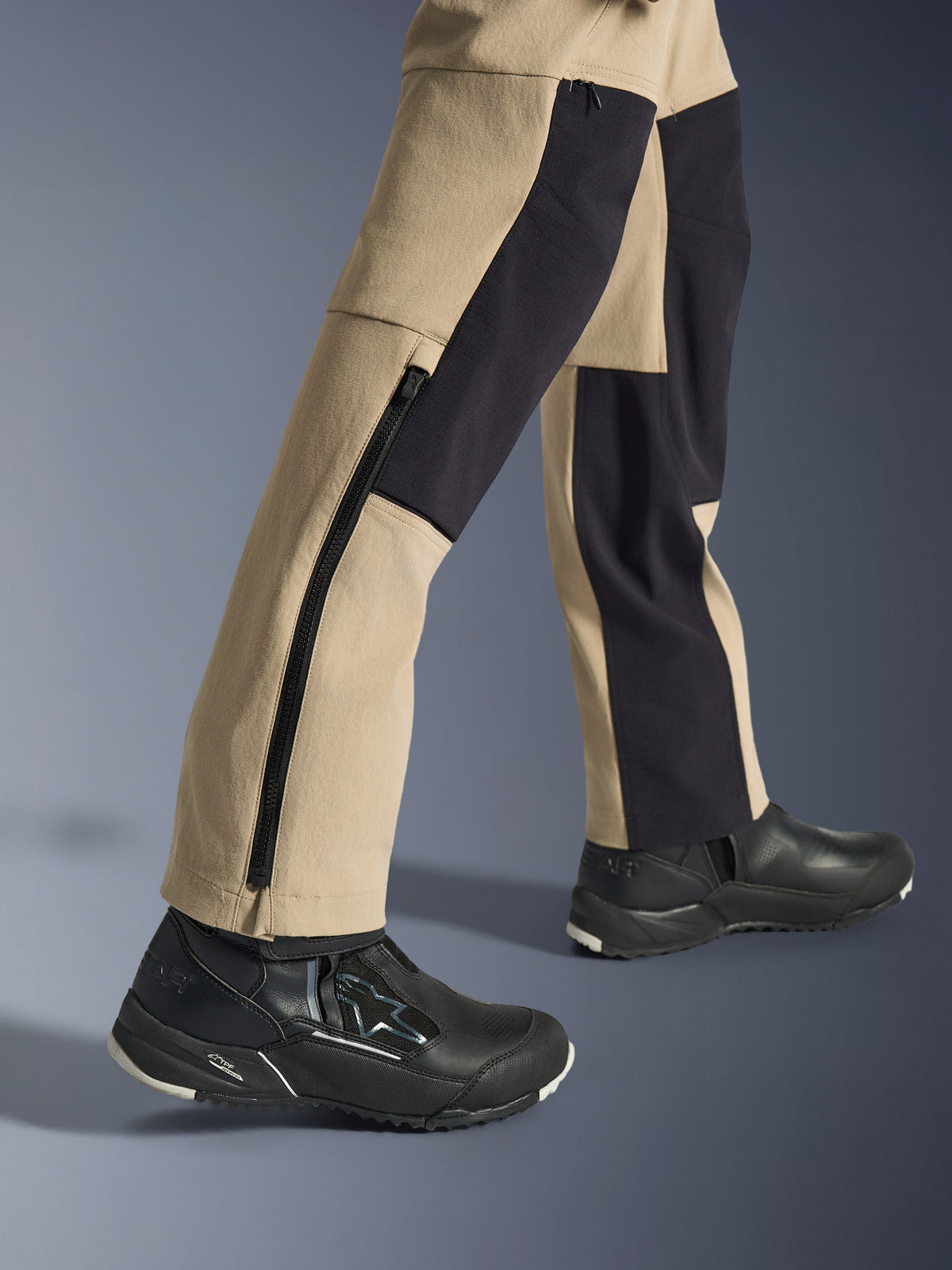 Alpinestars Stella Flex-AST Explorer dames motorbroek, adventure motorbroek, zandkleur en zwart, close-up van de onderbenen en enkels met een lange zijrits en zwarte verstevigingspanelen, gedragen met zwarte Alpinestars motorschoenen