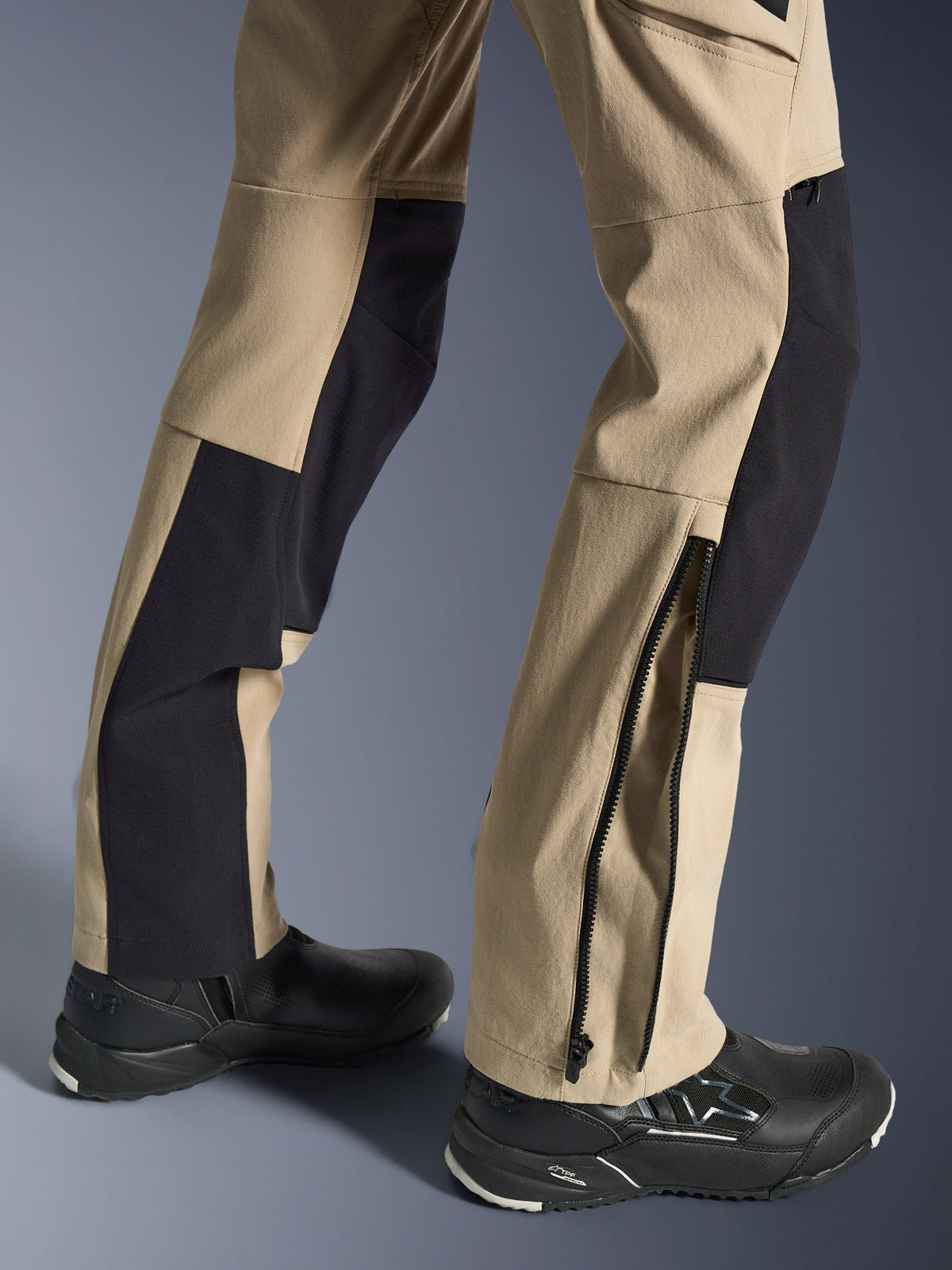 Alpinestars Stella Flex-AST Explorer broek, dames motorbroek, zandkleur en zwart, close-up van de onderbenen met een ritssluiting bij de zoom voor pasvorm over laarzen, gedragen met zwarte Alpinestars motorschoenen, voorzien van duurzame ripstop en ademende stretchstof panelen.