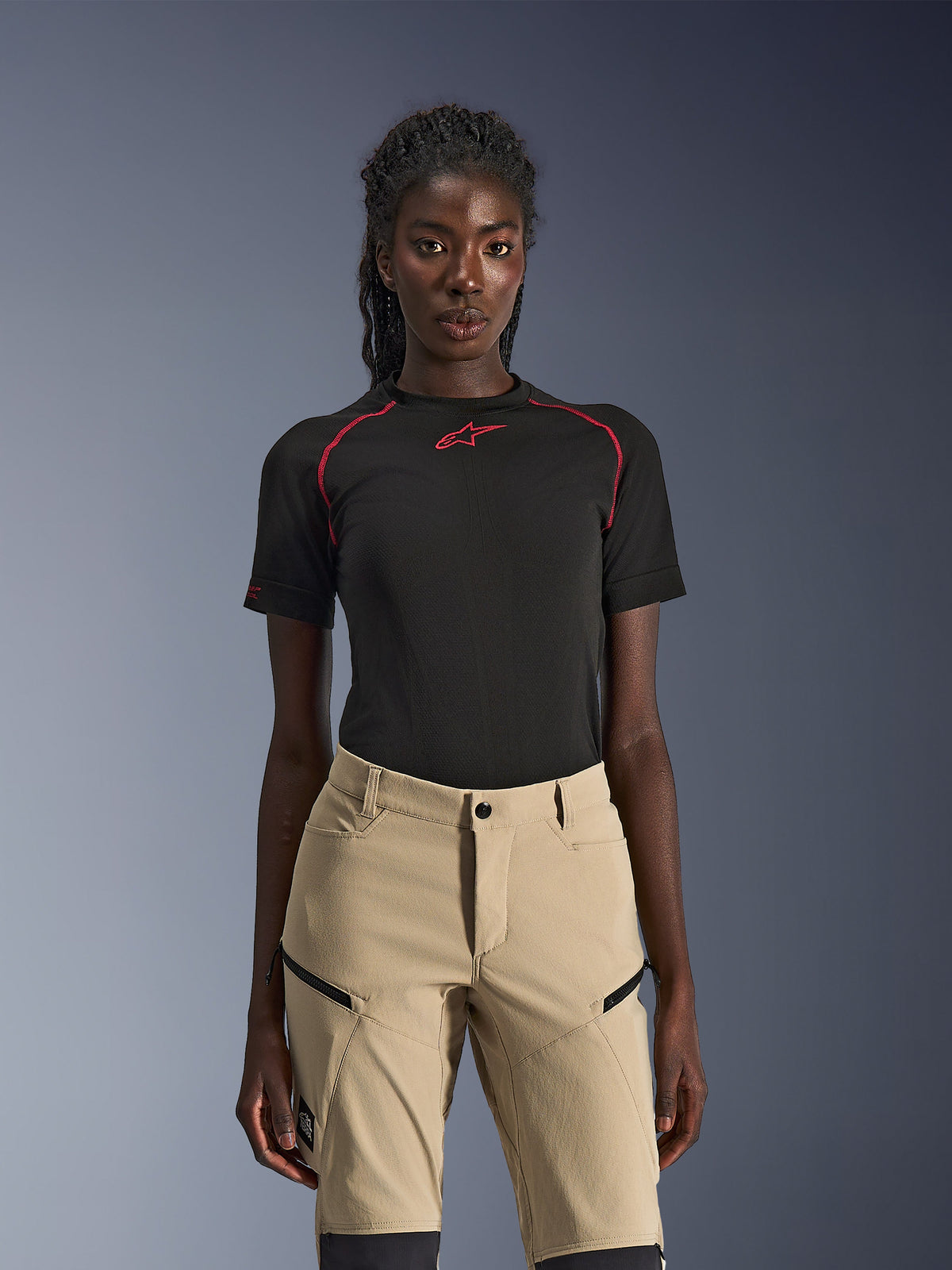 Alpinestars Stella Flex-AST Explorer Pants, dames motorbroek in zandkleur, gedragen met een zwarte technische top met korte mouwen en rode stiksels, adventure touring kleding voorzien van cargozakken met ritssluiting en duurzame ripstop stof