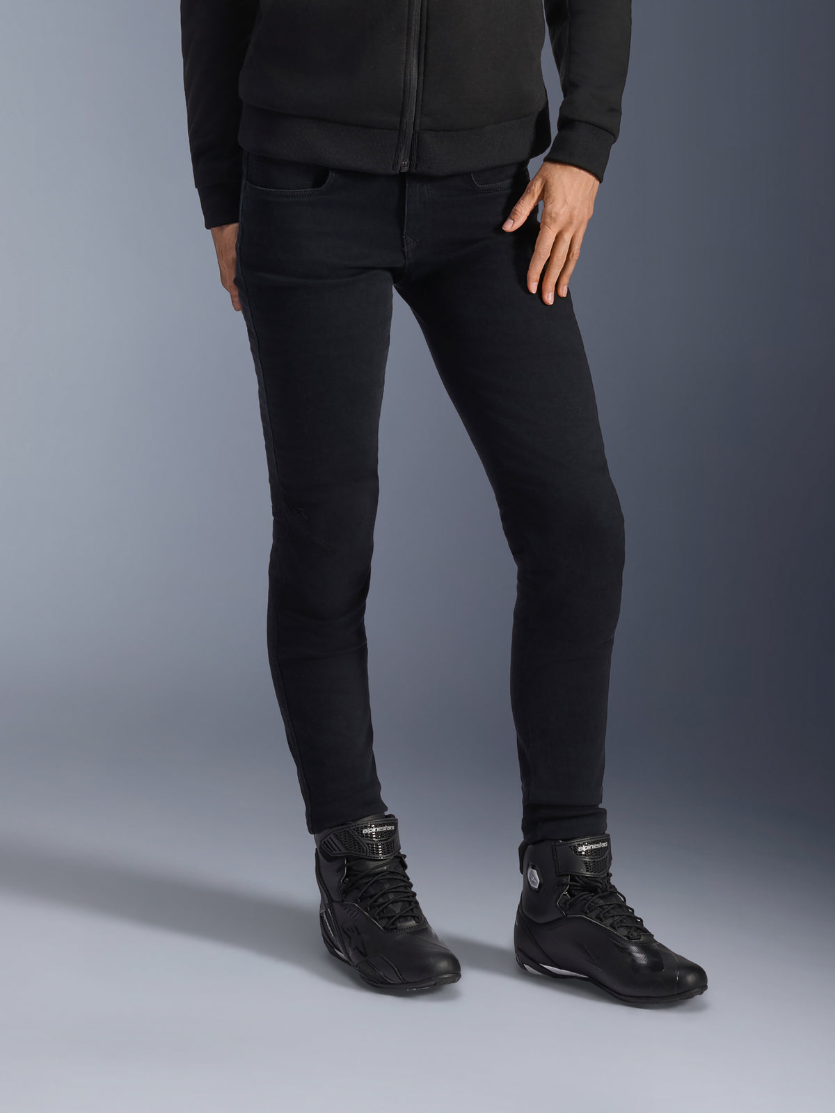 Alpinestars Daisy V3, jean de moto pour femme, noir, coupe ajustée, porté avec des bottines de moto montantes et un sweat à capuche zippé noirs, style urbain monochrome épuré