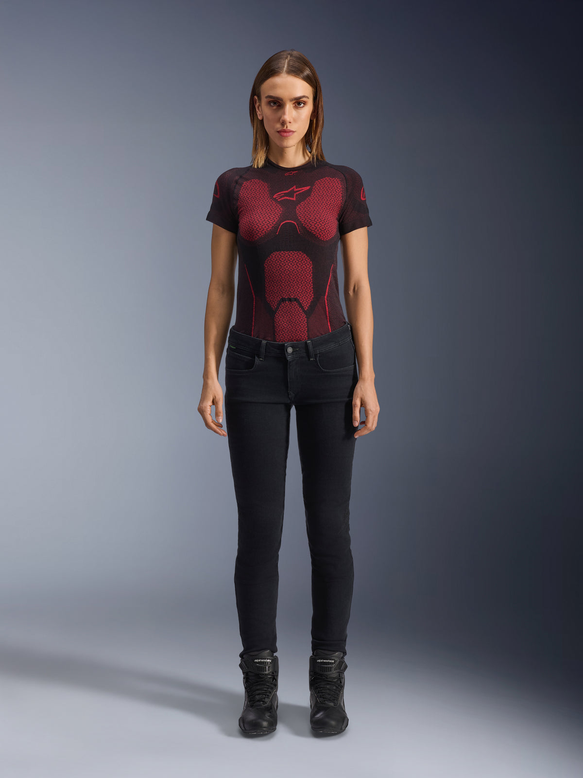 Alpinestars Daisy V3 Women's Riding Denim, Noir, pantalon de moto coupe slim, porté par un mannequin avec un t-shirt technique à motifs rouges et noirs et des bottes de moto noires, équipement urbain décontracté avec une silhouette féminine et une taille haute.