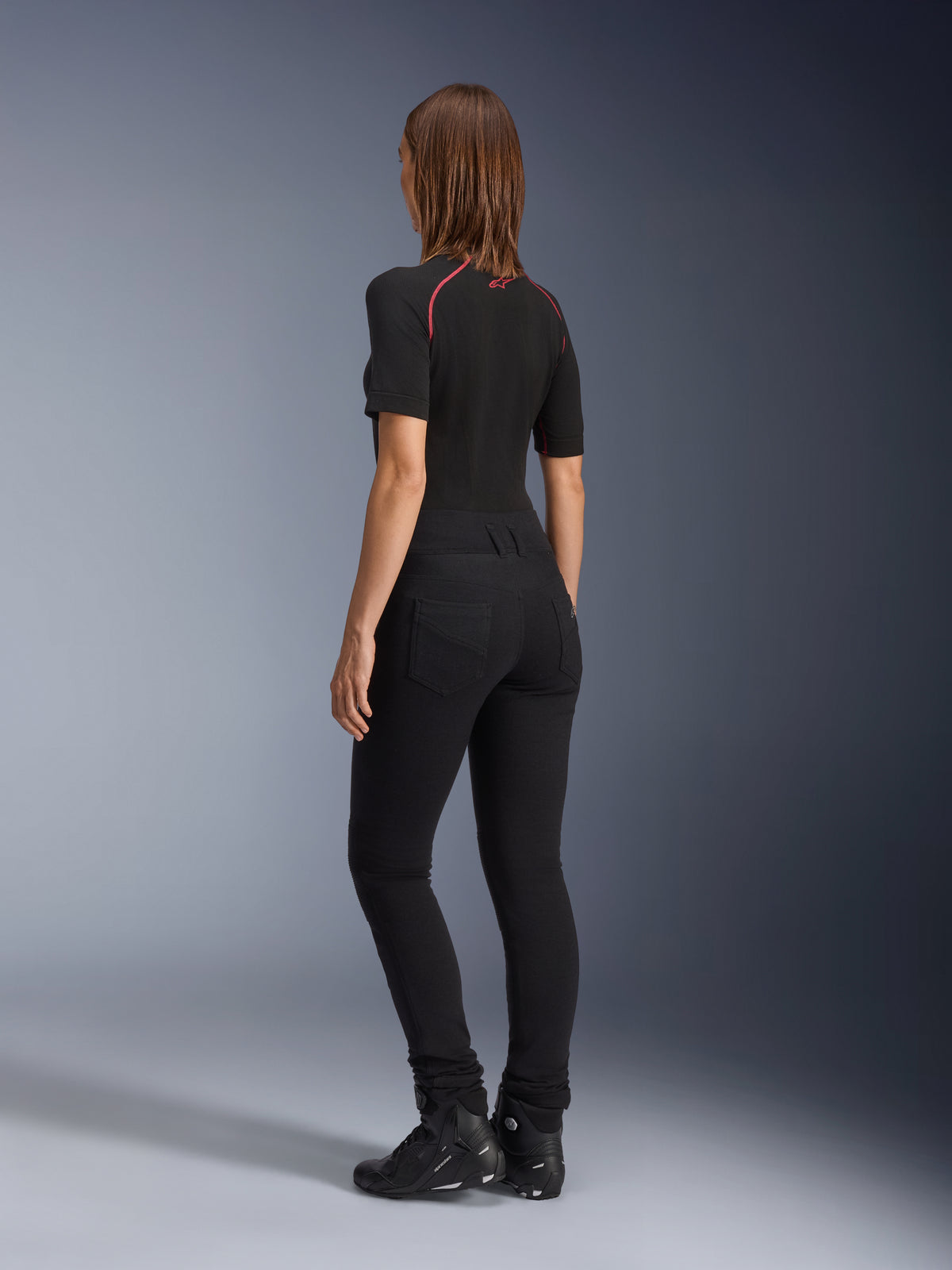 Alpinestars Damen-Banshee Leggings, Schwarz, Rückansicht mit figurbetonter anatomischer Stretch-Passform und Gesäßtaschen, getragen mit schwarzem Kurzarm-Oberteil und Motorradstiefeln, elegante urbane Motorradausrüstung für Damen