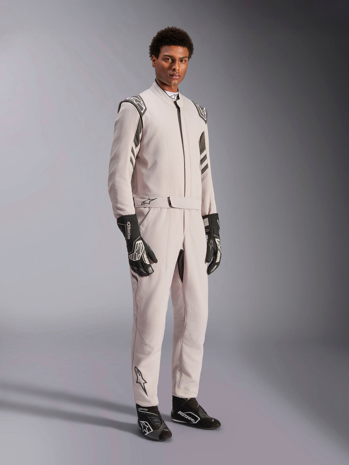 Alpinestars GP Race V3 Suit FIA, Silver Anthracite racing suit, one-piece driver suit with shoulder epaulettes and a belted waist, worn with matching black and white racing gloves and boots, sleek design for professional auto racing