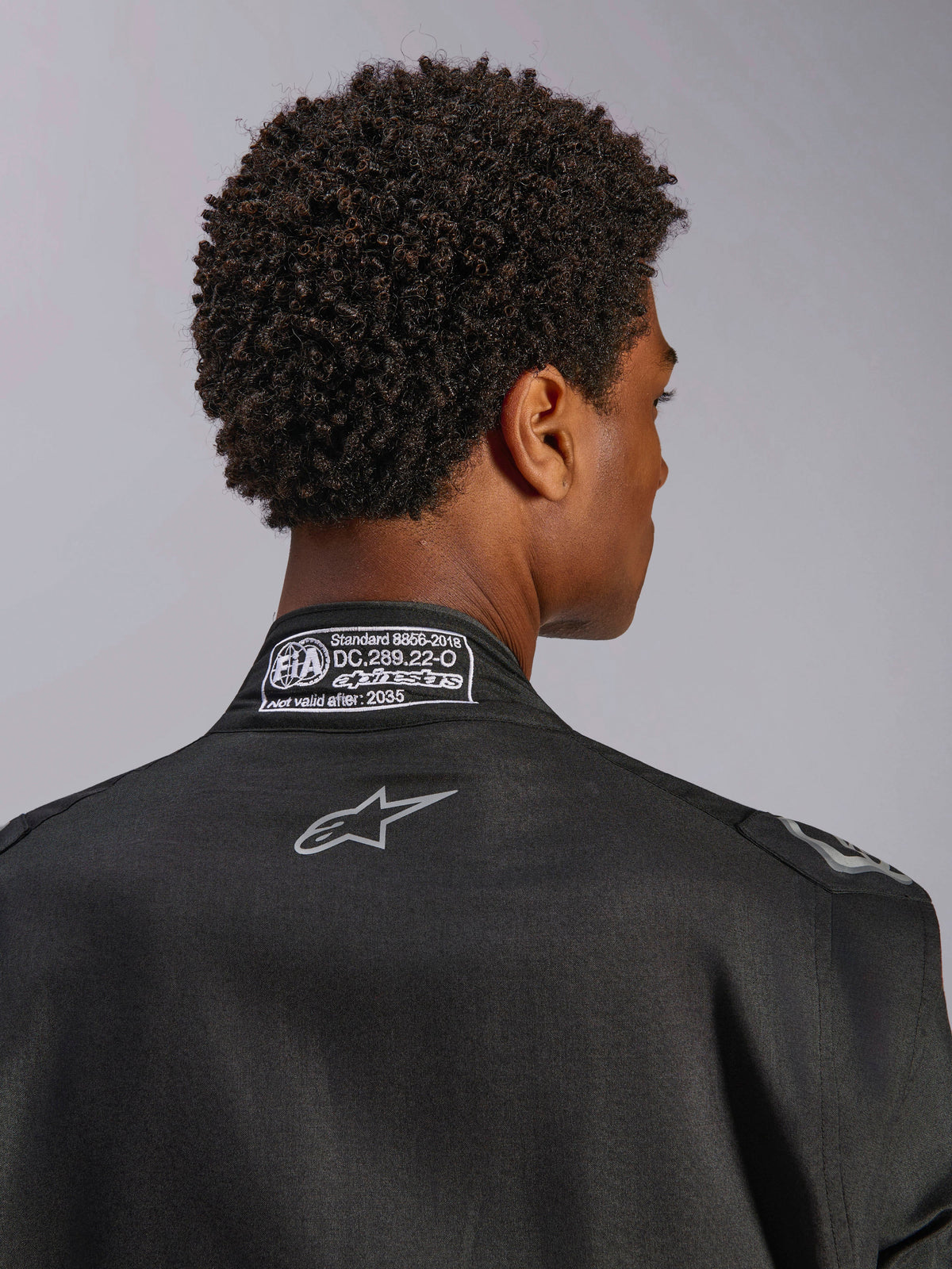 Combinaison Alpinestars Hypertech V3, Noir Dark Shadow, vue arrière rapprochée du col avec étiquette d'homologation FIA 8856-2018 et logo dorsal, combinaison de course professionnelle légère avec coupe athlétique