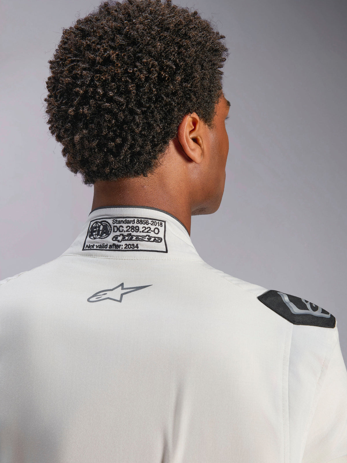 Alpinestars Hypertech V3 Pak, wit, detailweergave van de kraag en schouder aan de achterzijde, voorzien van FIA 8856-2018-certificeringslabel, geprint grijs Alpinestars-logo en zwarte extractiehandgreep, professionele race-uitrusting