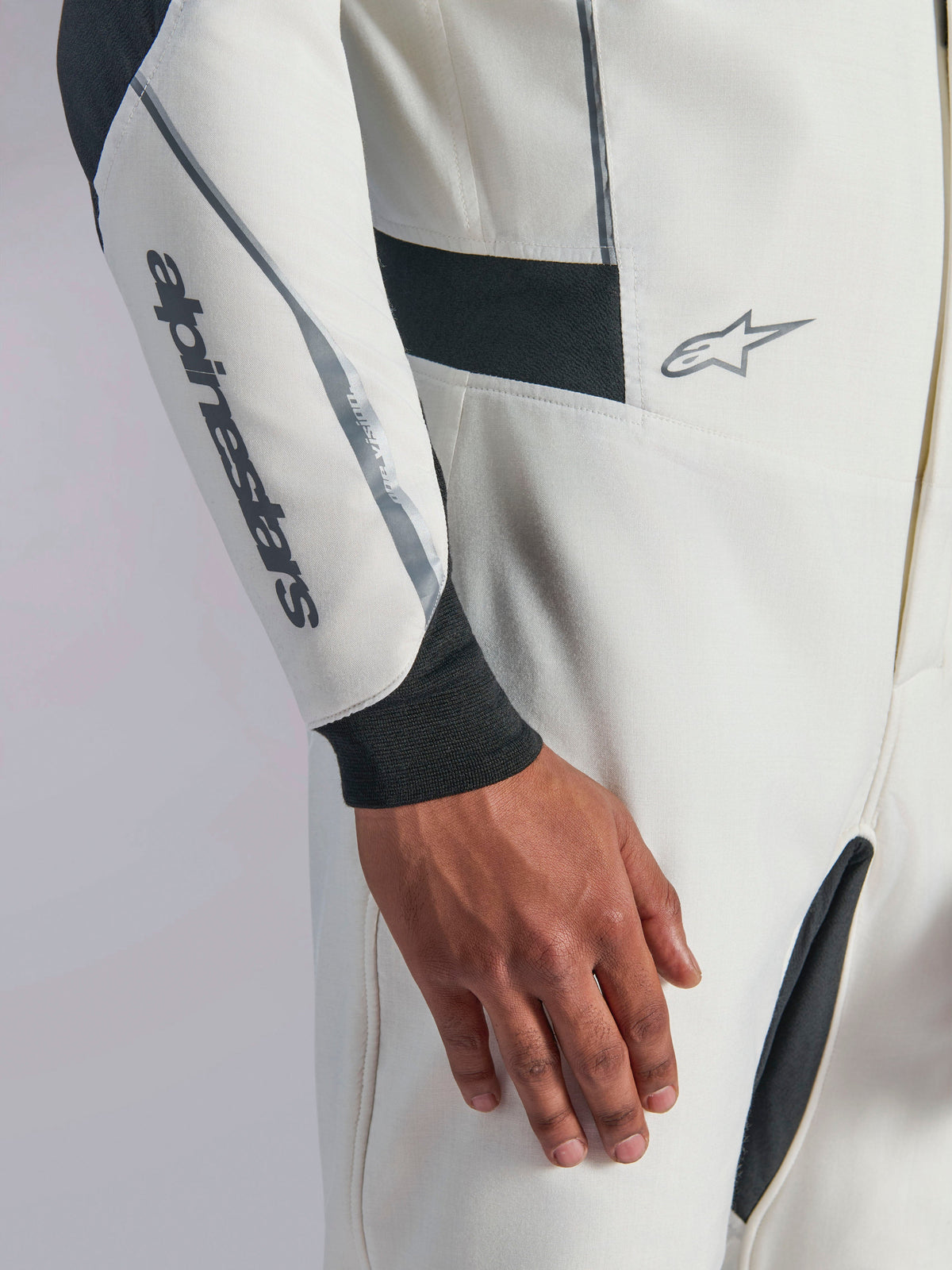 Alpinestars Hypertech V3 Pak, close-up van wit autoracepak met zwarte en zilveren accenten, Alpinestars-logo op de onderarm, zwarte gebreide polsmanchet, donkere stretchpanelen voor bewegingsvrijheid, professionele motorsportkleding