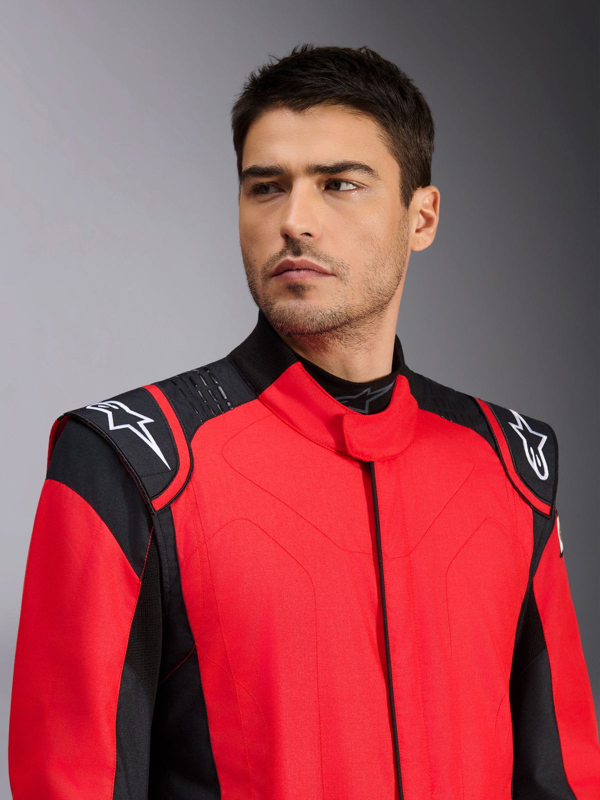 Männliches Model im Alpinestars GP Pro Comp V2 FIA Auto-Rennanzug, Rot und Schwarz, mit weißen Astars-Logos auf den Schultern und Silikon-Grip-Technologie-Details, professionelle Motorsportbekleidung