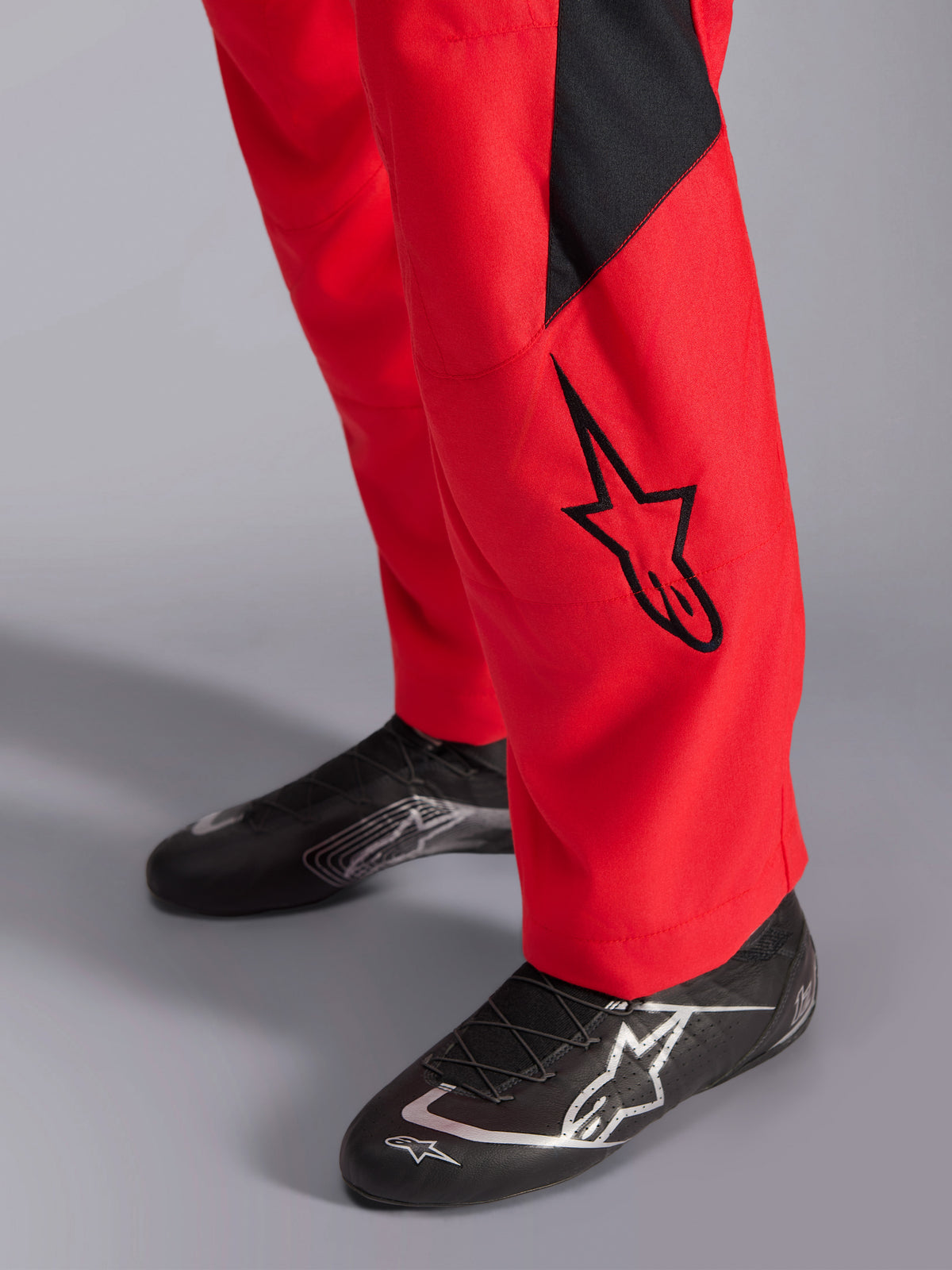 Alpinestars GP Pro Comp V2 FIA Rennanzug, Nahaufnahme des Unterschenkels und der Rennschuhe, Rot mit schwarzem Astars-Logo und Einsatz, kombiniert mit schwarzem Performance-Rennschuhwerk, Autorenn-Ausrüstung.
