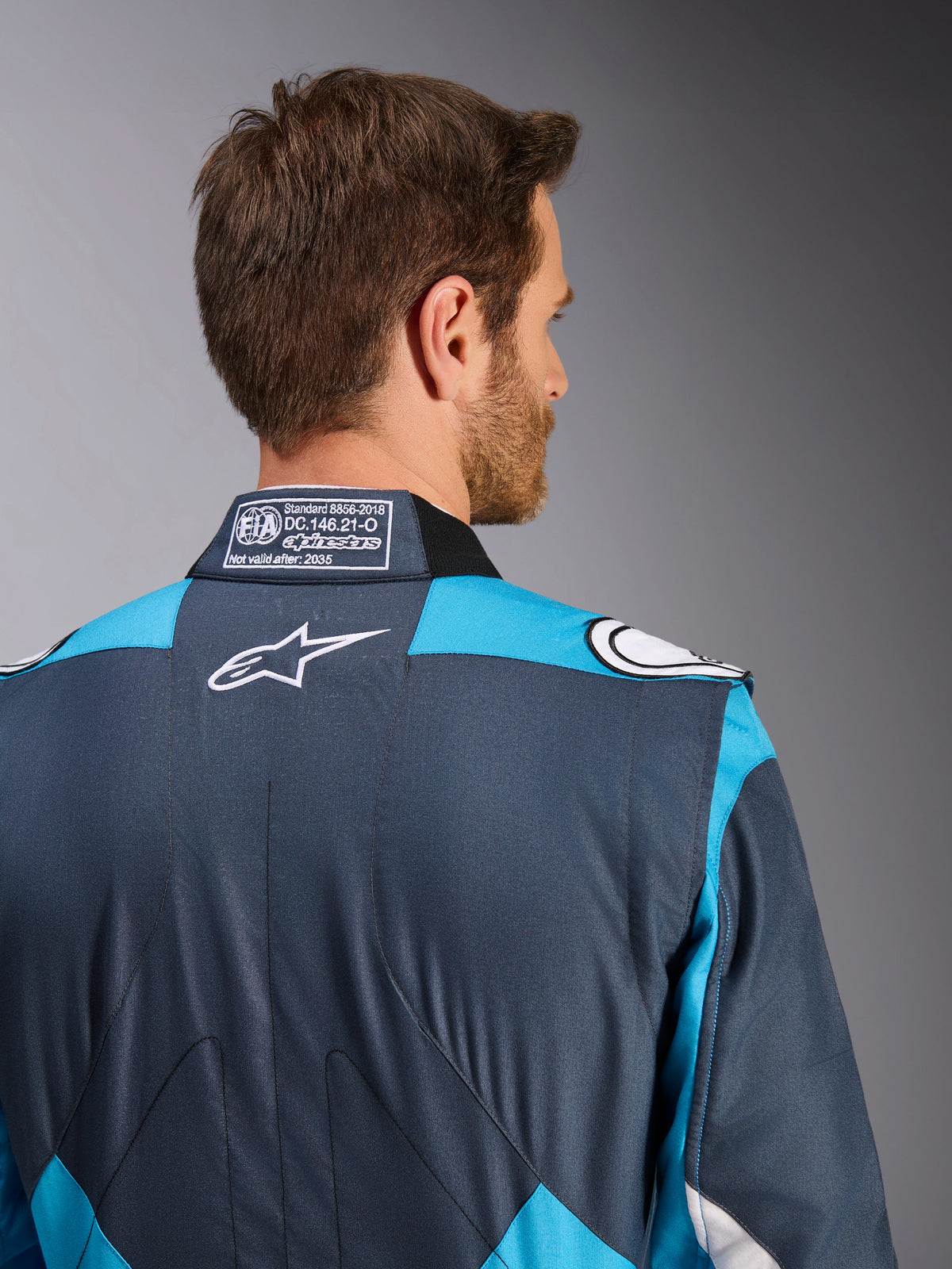 Alpinestars GP Pro Comp V2 Rennanzug für Herren in Asphalt und Cyan, mit FIA-Kragenetikett und weißem Logo auf dem Rücken.