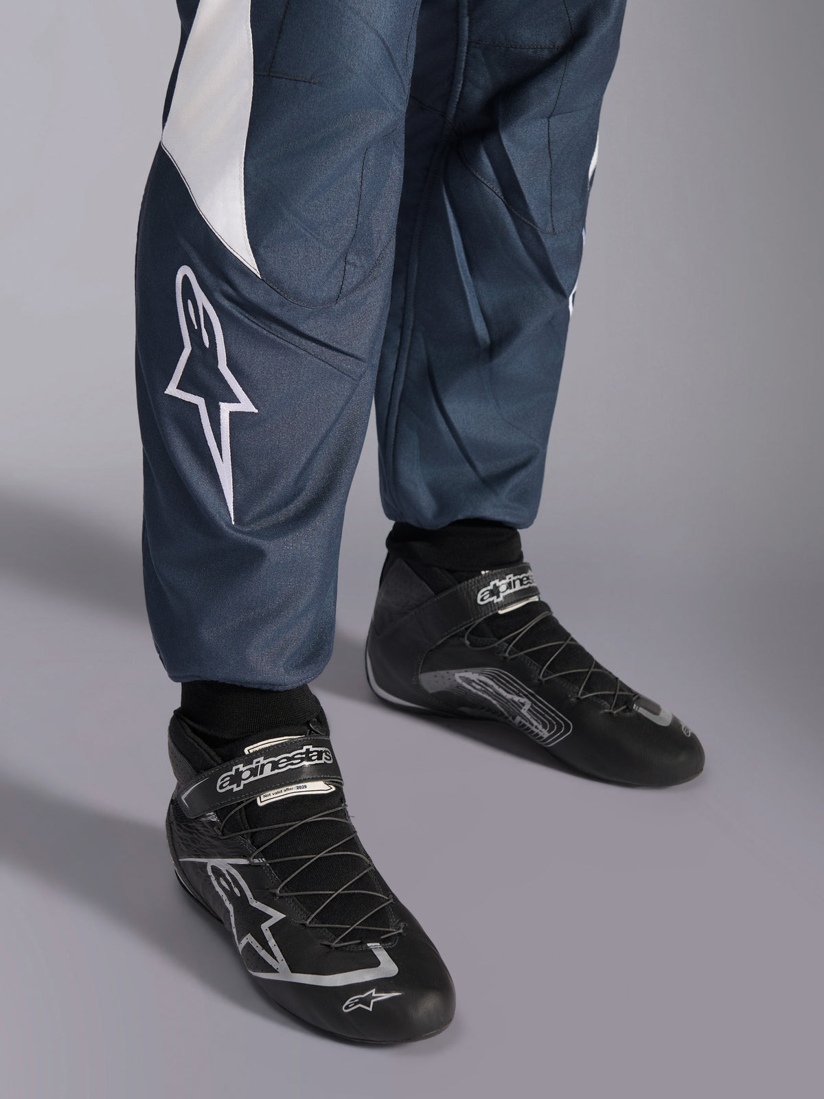 Alpinestars GP Pro Comp V2 Kombi, FIA-zertifizierter Auto-Rennanzug in Asphalt und Cyan, Detail mit schwarzen Rennschuhen.