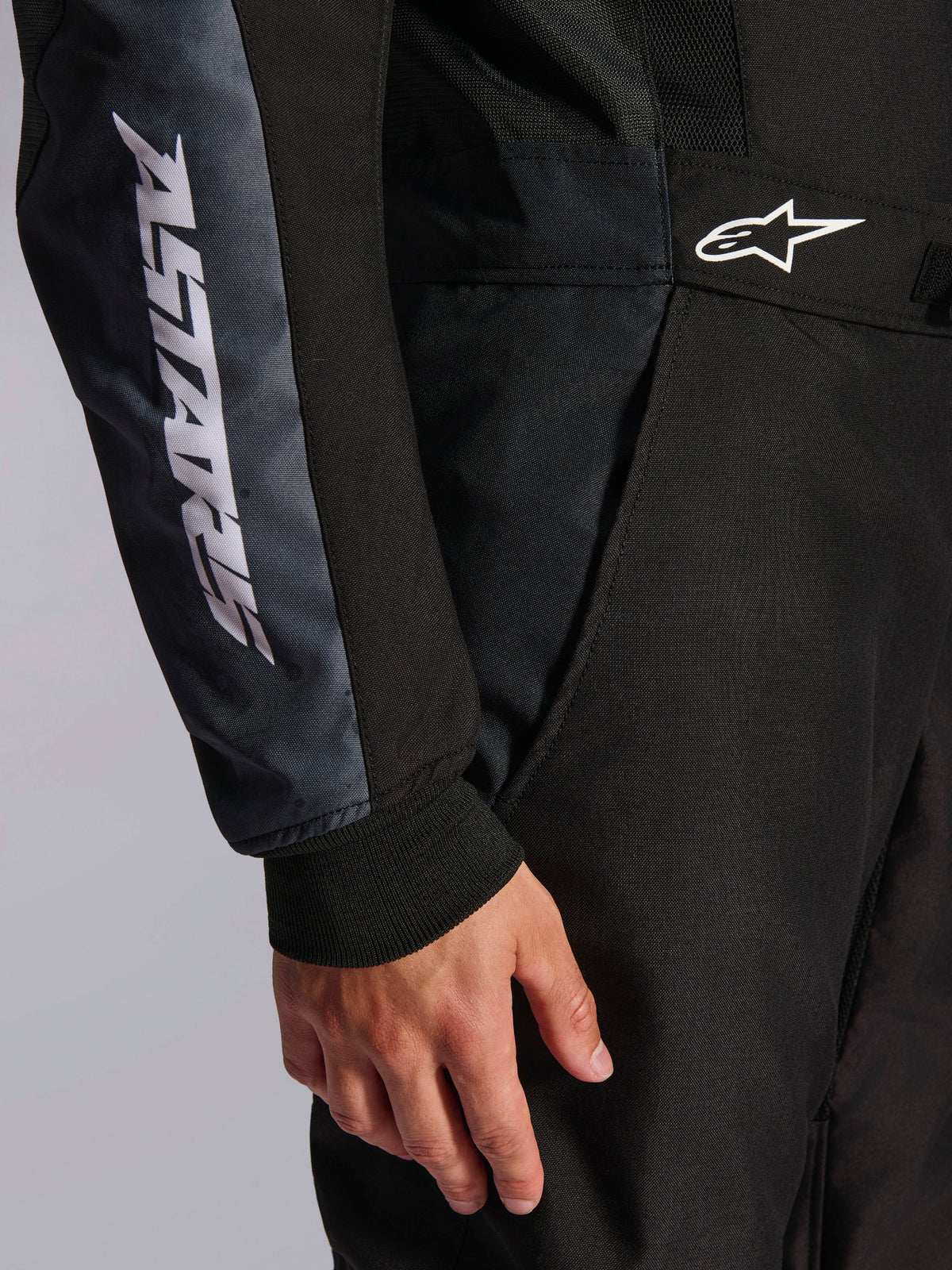 Combinaison Alpinestars KMX-5 V3, combinaison de karting, noir et Dark Shadow, gros plan sur le côté de la hanche et le bras, marquage ASTARS blanc sur la manche, logo blanc à la taille, avec panneaux en mesh pour la ventilation et poignet en tricot
