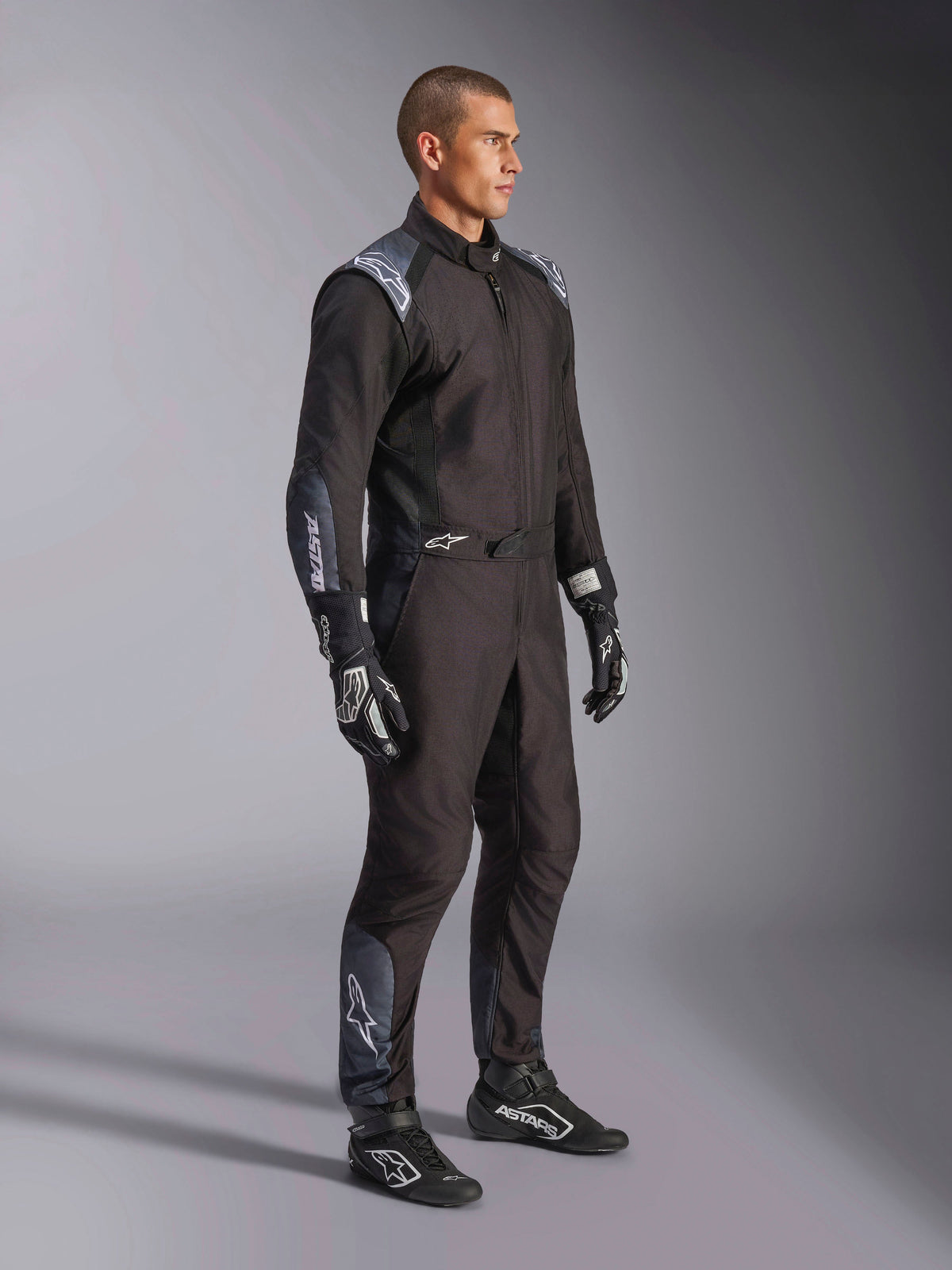 Combinaison Alpinestars KMX-5 V3, combinaison de karting en Black Dark Shadow, portée avec des gants et des chaussures de course noirs assortis, dotée de perforations découpées au laser et de panneaux en mesh technique, design épuré à double couche avec logos blancs pour le sport automobile professionnel