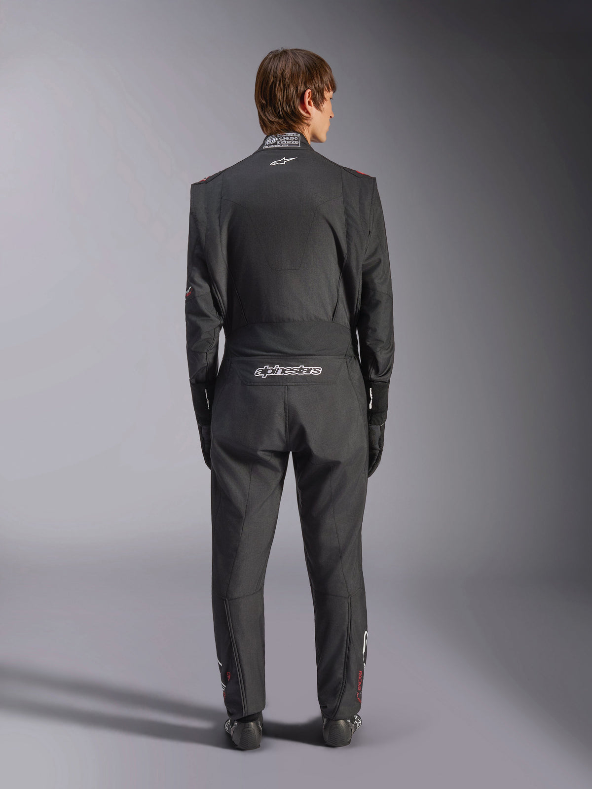 Alpinestars GP Tech V4-pak, autoracepak, zwart en wit, achteraanzicht met witte Alpinestars-branding en FIA-certificering op de kraag, gestroomlijnde ergonomische pasvorm voor professionele bescherming van de coureur