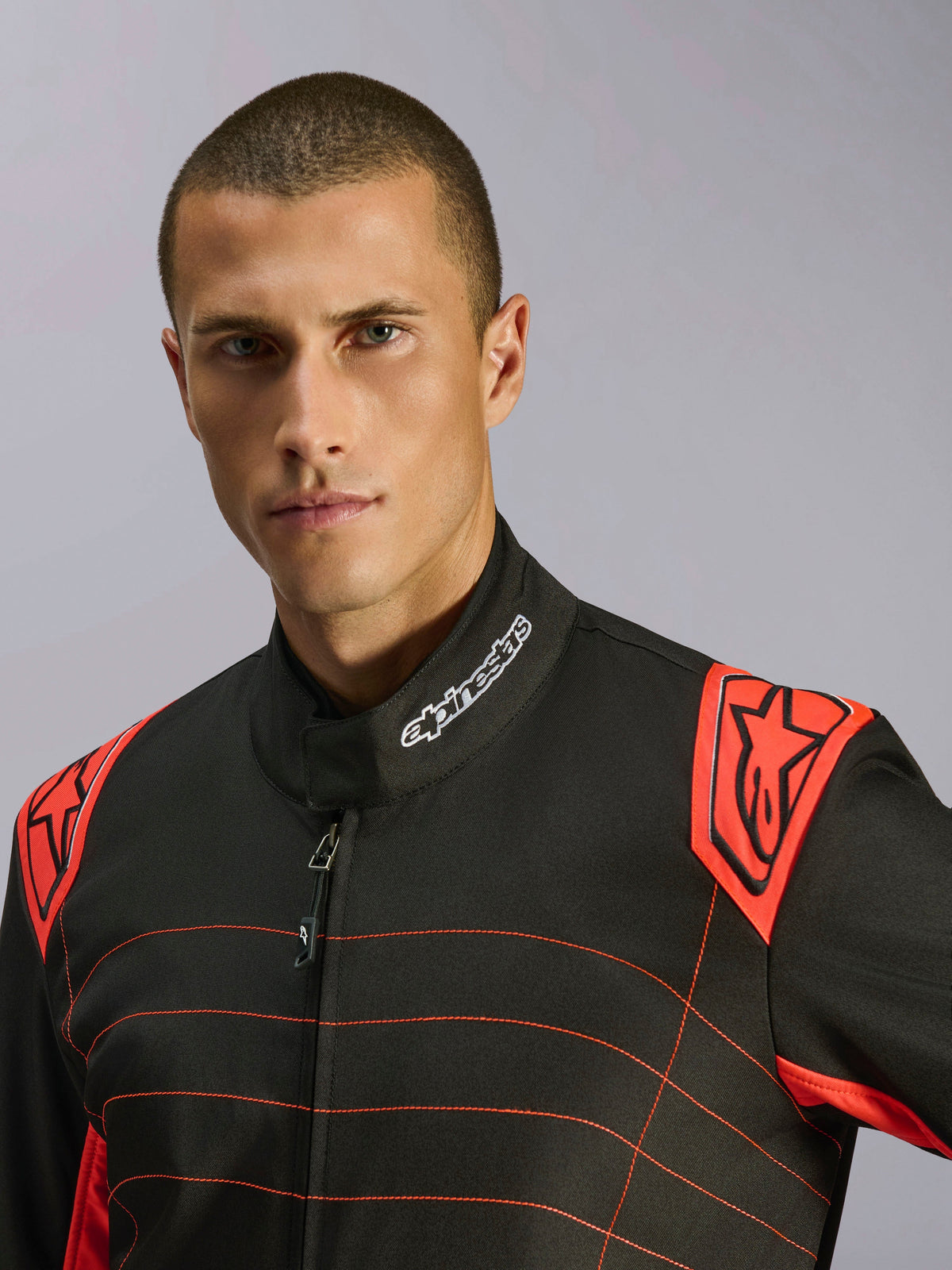 Nahaufnahme eines Fahrers im Alpinestars KMX-9 V3 Anzug in Schwarz und Neonrot, mit einem gestickten Logo am Kragen und roten Schulterepauletten mit Alpinestars-Branding, technisches Design für den Kartsport