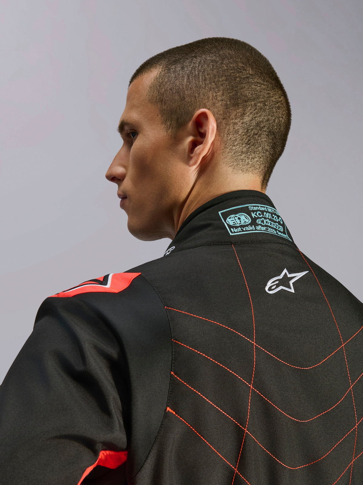 Alpinestars KMX-9 V3 Anzug, Schwarz und Rot Fluo Kartanzug, Nahaufnahme des oberen Rückens und Kragens an einem Modell, mit weißem Alpinestars-Logo, detaillierten roten Nähten und FIA-Zertifizierungsetikett am Nacken