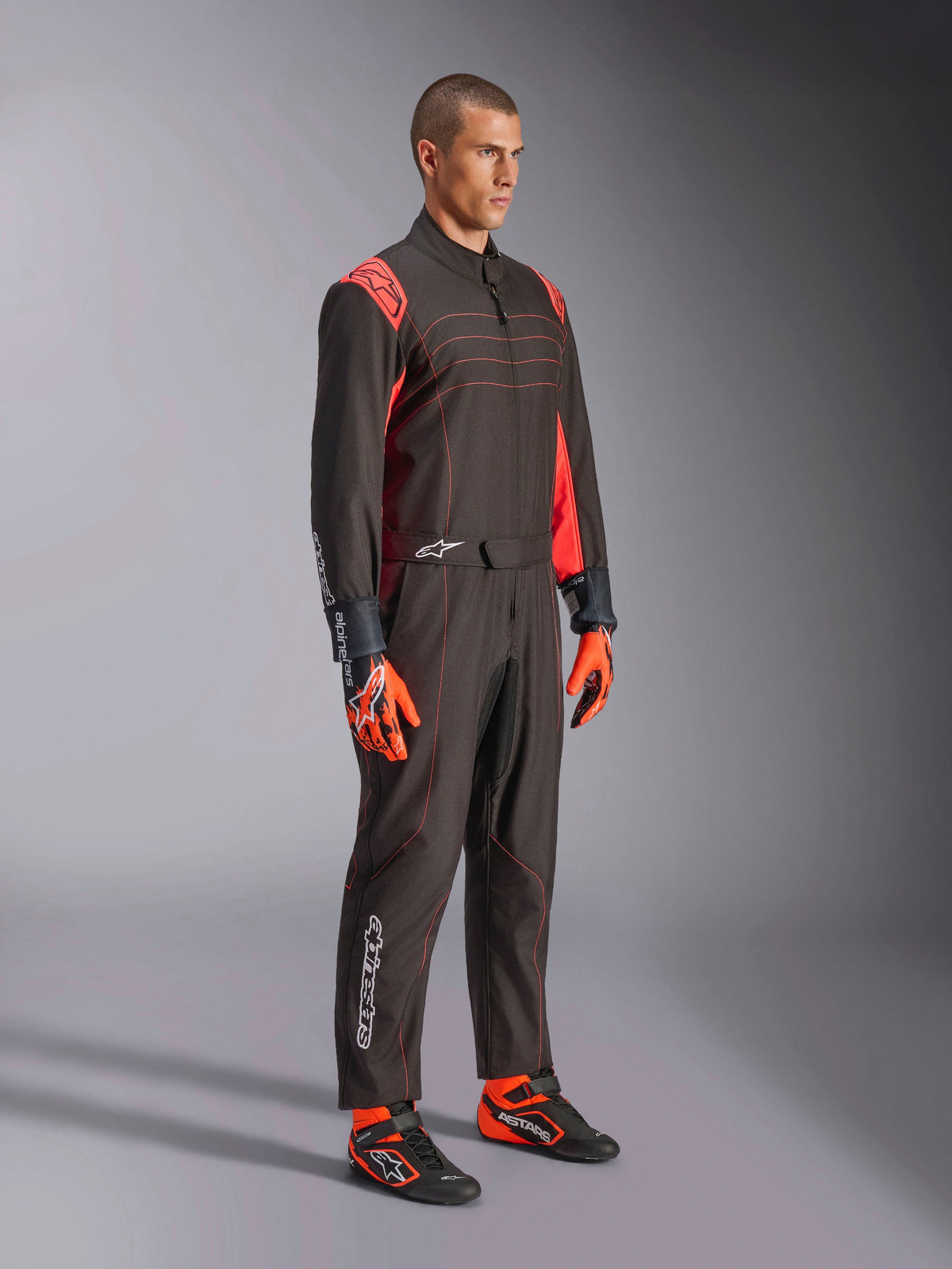Alpinestars KMX-9 V3 Anzug, Karting-Anzug, Schwarz Rot Fluo, getragen von einem Modell mit orangefarbenen Handschuhen und schwarzen Rennschuhen, mit roten Nähten, Schulterakzenten und weißen Logos, athletisches Design für professionellen Rennsport