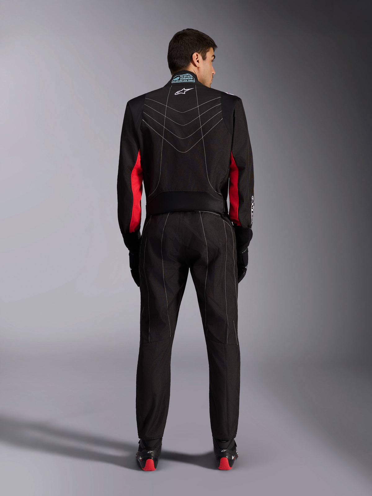 Alpinestars KMX-9 V3 Pak, kartpak, zwart met rode en witte accenten, volledig achteraanzicht, voorzien van witte V-vormige contraststiksels, rode panelen op de mouwen en Alpinestars-logo op de kraag, gecombineerd met zwarte racehandschoenen en schoenen