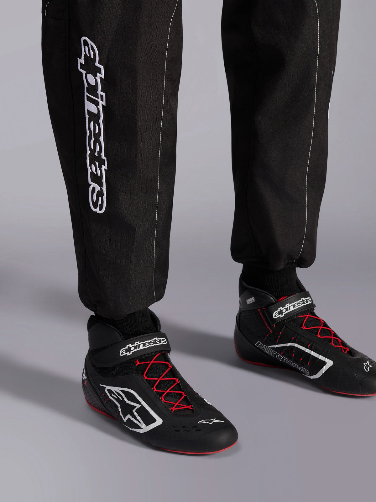 Alpinestars KMX-9 V3 Pak, kartpak, zwart rood en wit, detailweergave van de onderbenen en kartschoenen, witte Alpinestars-branding op de zijkant, zwarte schoenen met rode veters en witte accenten, professionele motorsportuitrusting