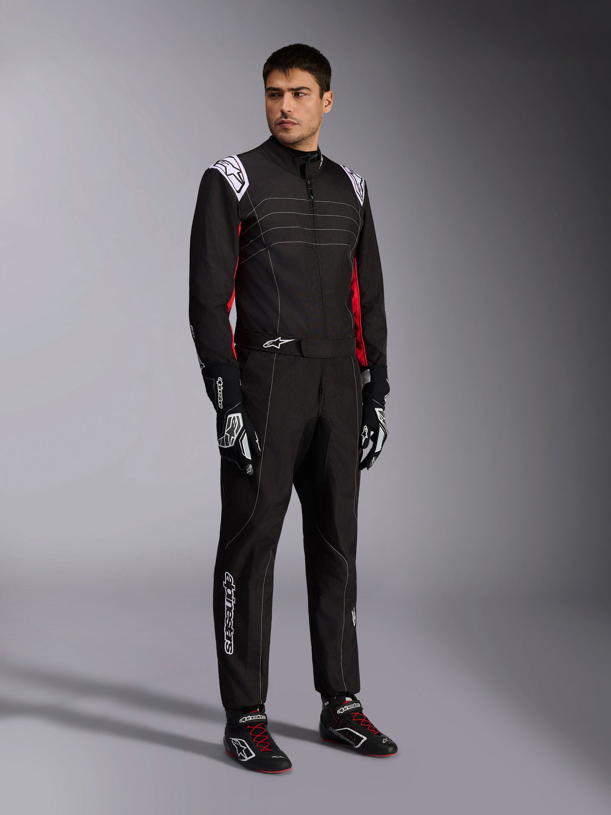 Alpinestars KMX-9 V3-pak, zwart, rood en wit kartingpak gedragen door een model, voorzien van witte epauletten en logo's, rode zij-accenten, gecombineerd met bijpassende racehandschoenen en schoenen, professionele motorsportkleding
