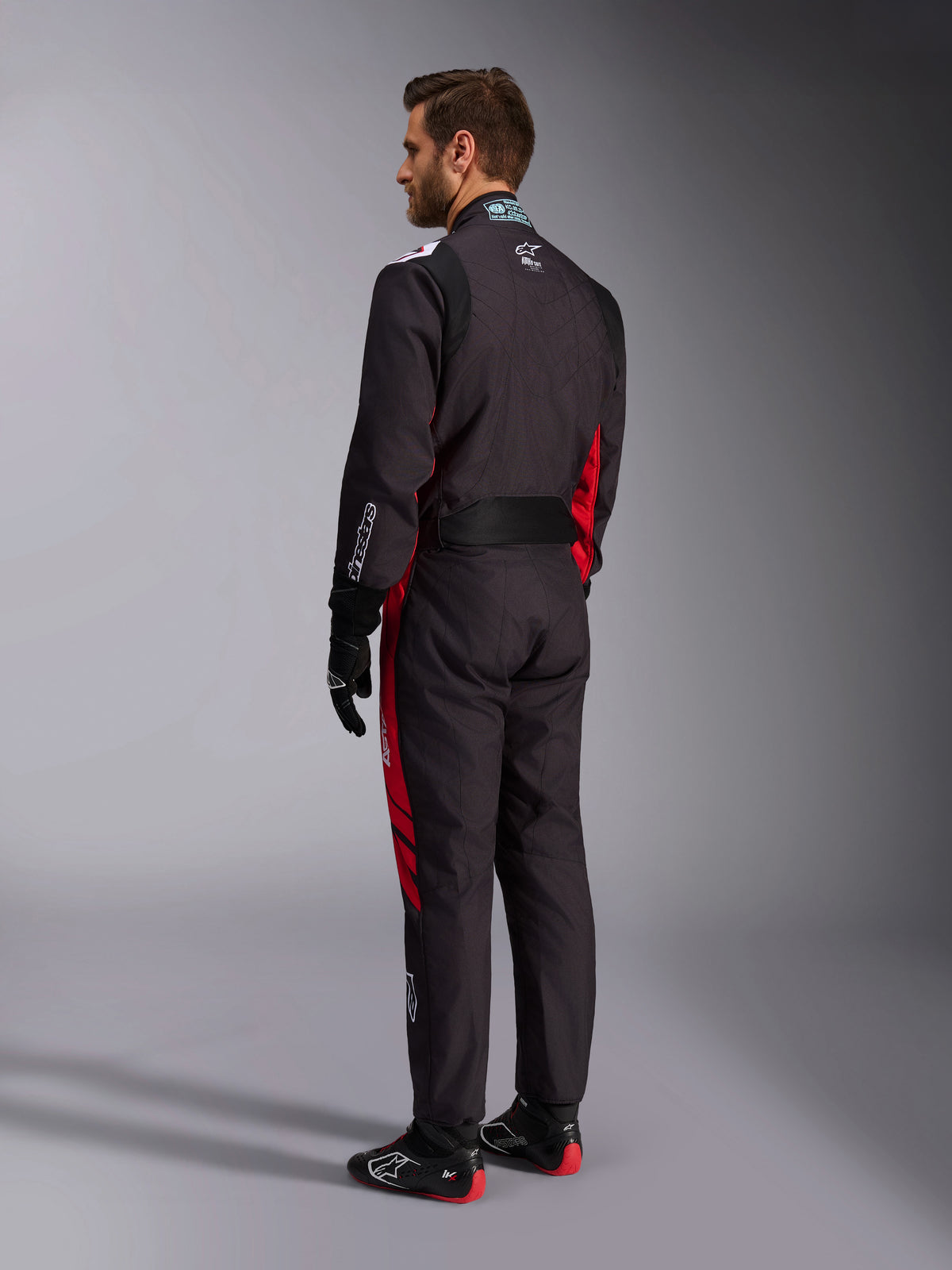 Alpinestars KMX-9 V3 Graphic 3 Suit, Black and Red, back view of model wearing full karting gear including black gloves and racing boots, featuring red side panels and white logo details