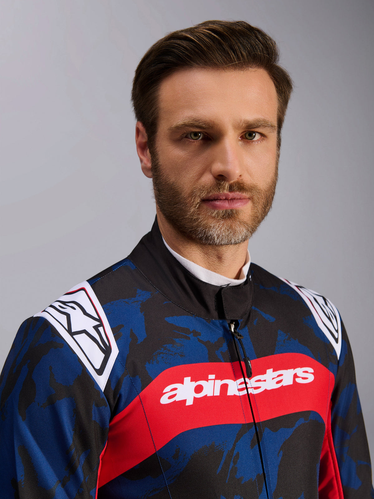 Combinaison Alpinestars KMX-9 V3 Graphic 5, combinaison de karting bleu marine et rouge, dotée d'un motif graphique camouflage bleu et noir, d'une large bande horizontale rouge avec le texte alpinestars blanc sur la poitrine et de logos blancs sur les épaules, portée par un mannequin en studio.