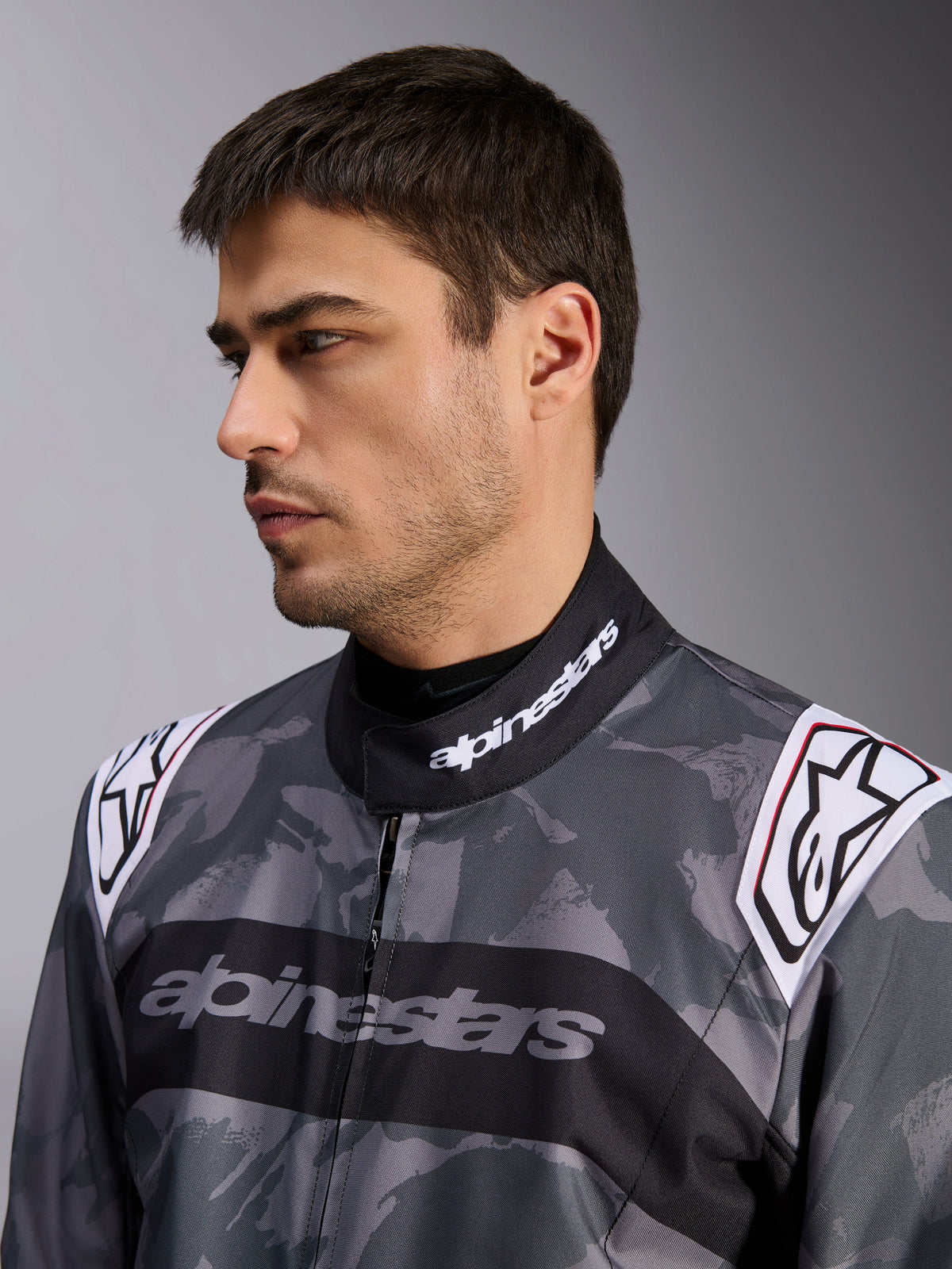Alpinestars KMX-9 V3 Graphic 5 Anzug, Kart-Anzug, dunkelgraues und schwarzes Camouflage-Muster, Nahaufnahme von Kragen und Schultern mit weißen Logos, professionelle Rennbekleidung