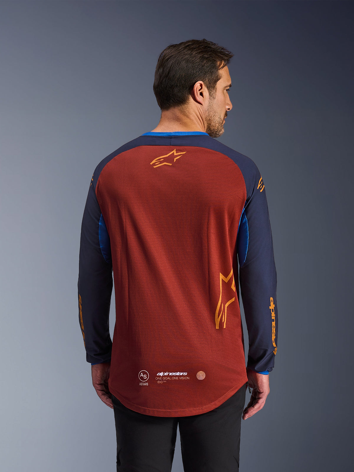 Maillot Alpinestars Maxdura Dual en brun rouille et bleu Mood Indigo, vue de dos, doté d'un torse en maille respirante, de manches bleu foncé avec marquage Alpinestars orange et d'un pan arrière allongé pour une protection accrue.