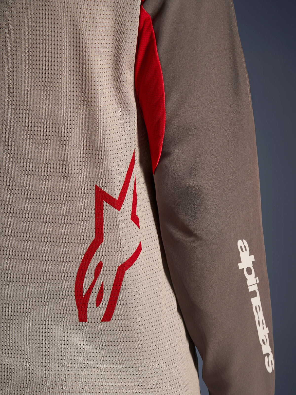 Alpinestars Maxdura Dual Jersey, Aluminum Walnut, close-up weergave van de torso van geventileerd mesh met een rood sterlogo en een bruine slijtvaste mouw met een wit Alpinestars woordmerk, technische adventure en dual-sport motorkleding