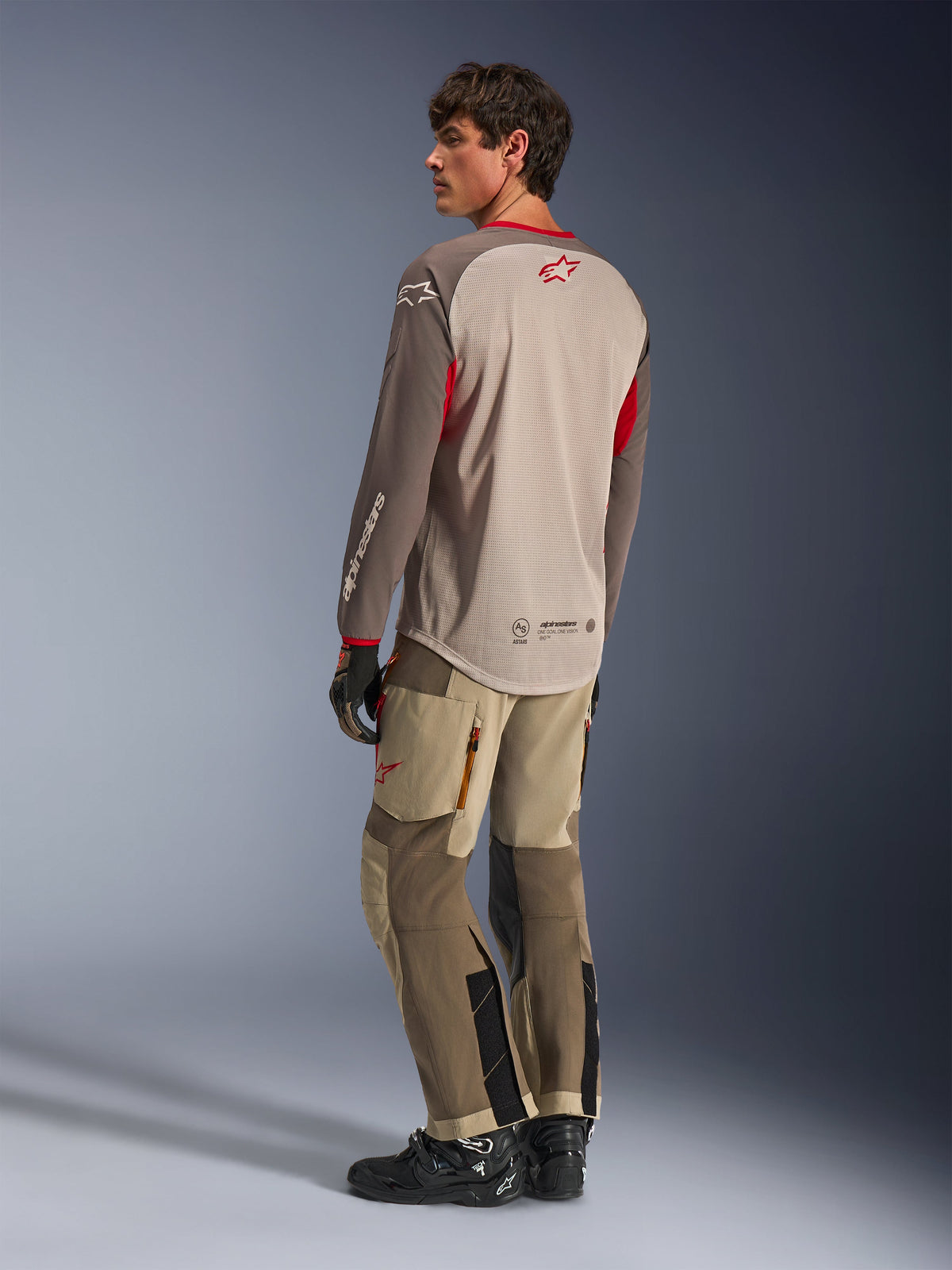 Alpinestars Maxdura Dual Jersey in Aluminum Walnut, achteraanzicht van adventure motorjersey met een ademende mesh torso en rode accenten, gecombineerd met bijpassende technische adventurebroek en zwarte laarzen