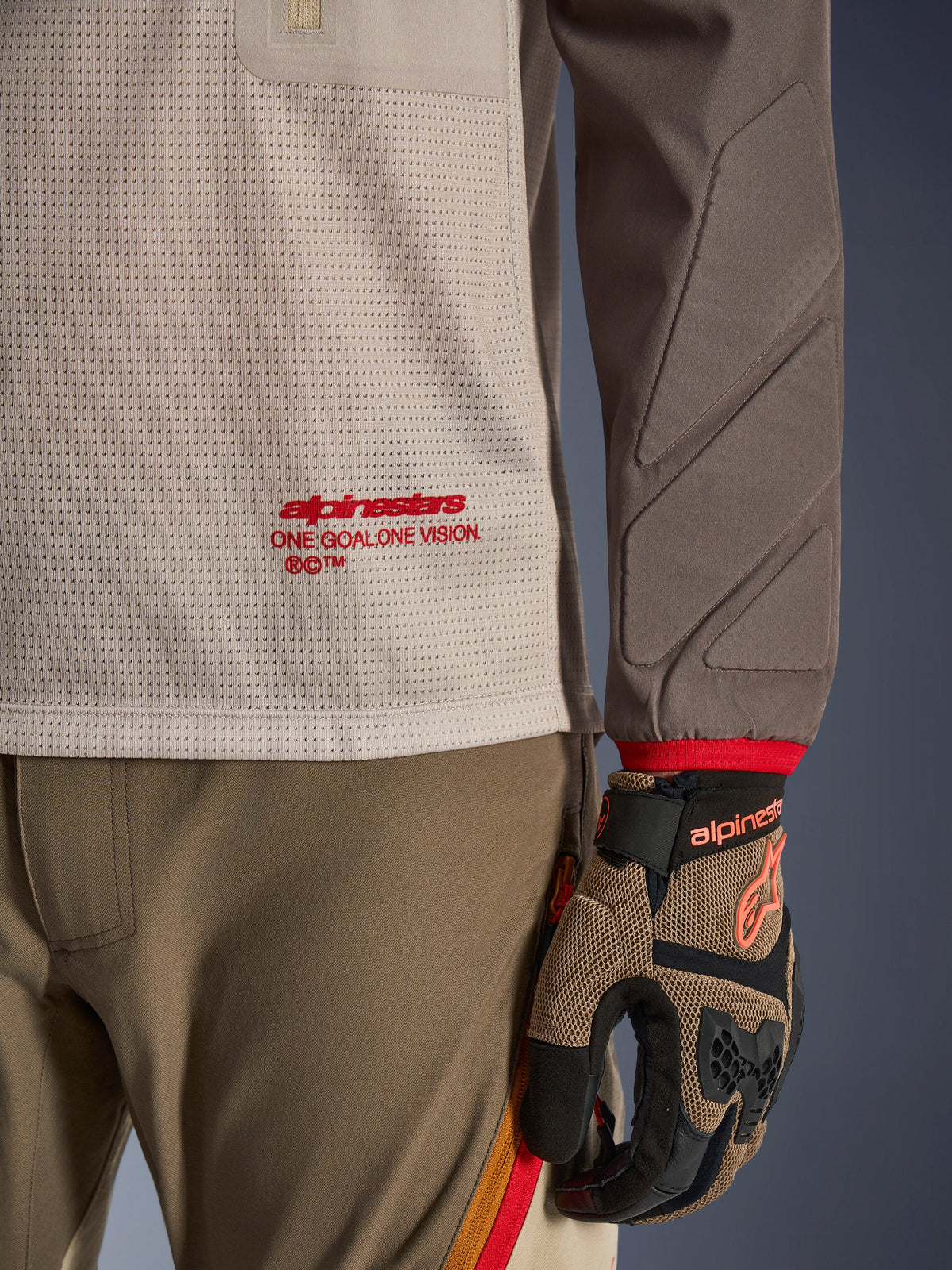 Alpinestars Maxdura Dual Jersey in Aluminum Walnut, detailweergave van de geventileerde mesh torso met rode branding, slijtvaste mouw met geïntegreerde padding, gedragen met bijpassende adventure motorbroek en handschoenen