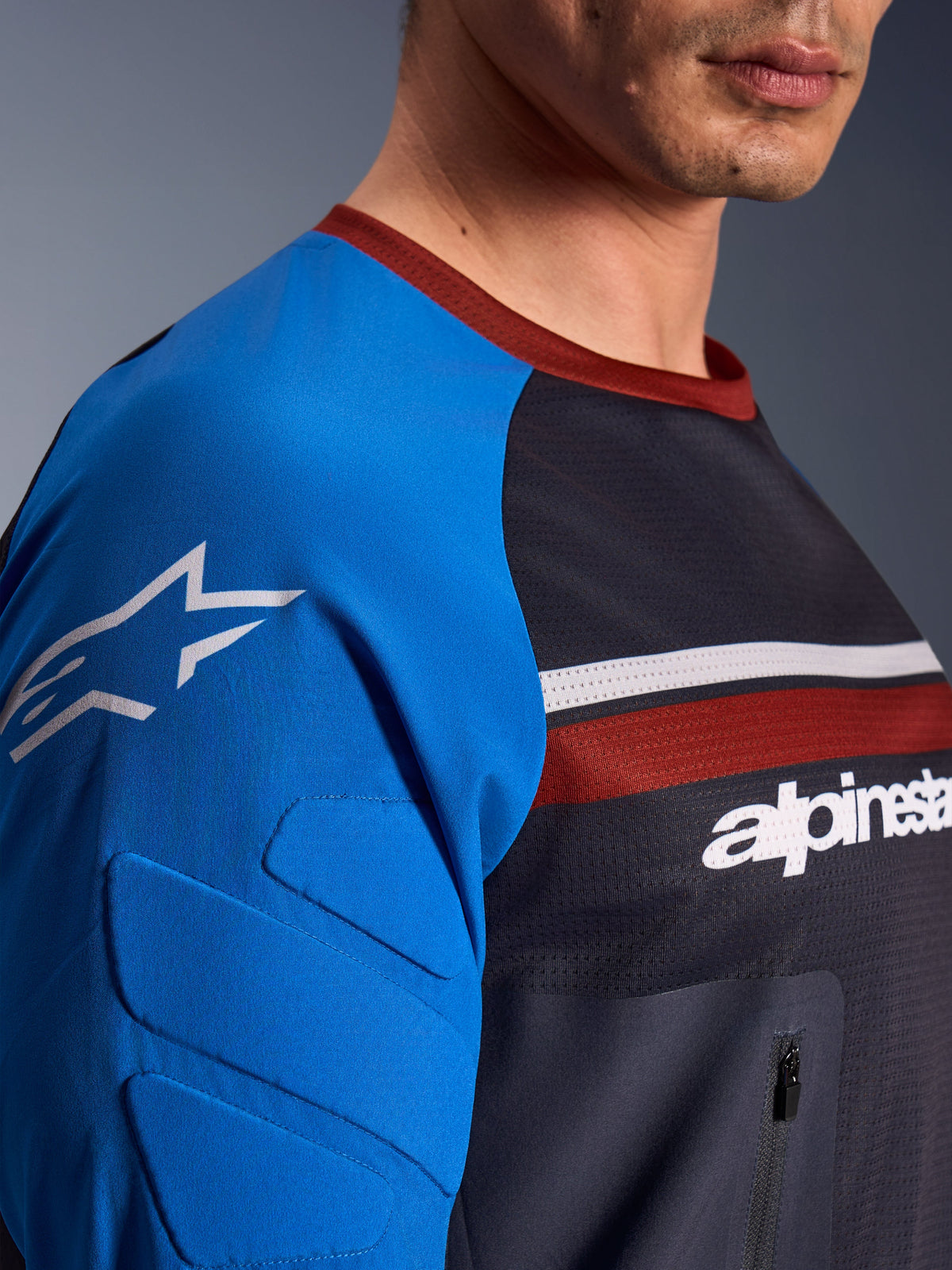 Alpinestars Maxdura Dual Jersey, maillot de moto, gris foncé et bleu royal, vue rapprochée montrant la poche poitrine zippée, le tissu en maille du torse et le rembourrage intégré aux manches avec logo étoilé