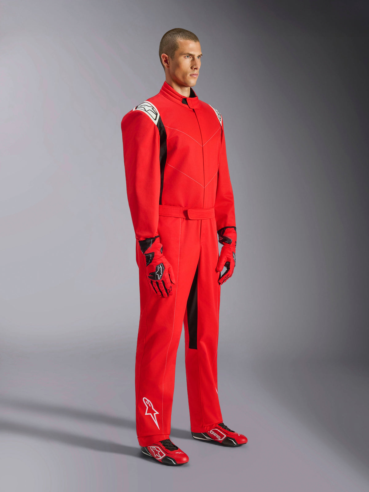 Alpinestars Kart Indoor V2 Anzug, roter Kart-Anzug, getragen von einem Model mit passenden rot-schwarzen Handschuhen und Schuhen, weiße Logos auf Schultern und Unterschenkel, schwarze Akzente, entwickelt für Freizeit-Kartfahren und Indoor-Strecken.
