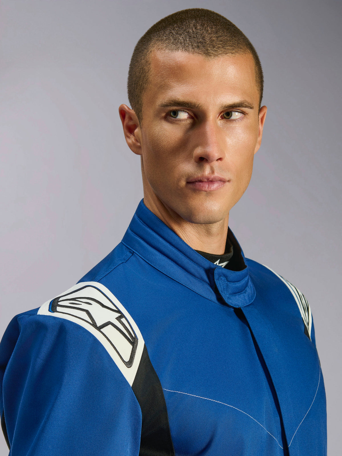 Alpinestars Kart Indoor V2 Anzug, blauer Kart-Anzug, Nahaufnahme eines männlichen Models, weiße Schulterpartien mit schwarzem Stern-Logo, ergonomischer Kragen, strapazierfähiger einlagiger Twill für den Freizeit-Rennsport.