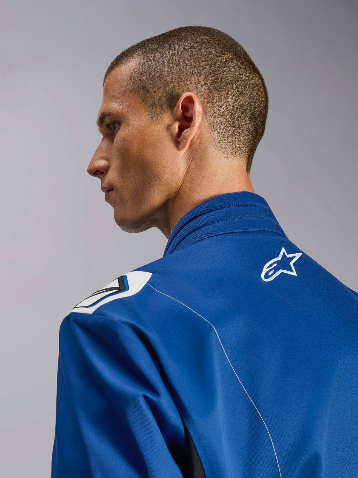 Alpinestars Kart Indoor V2 Anzug, blauer Kart-Anzug, Nahaufnahme des Seitenprofils mit ergonomischem Kragen und oberem Rücken mit weißem Stern-Logo, Formel-1-inspiriertes Schulterdesign und strapazierfähige Poly-Baumwoll-Twill-Konstruktion